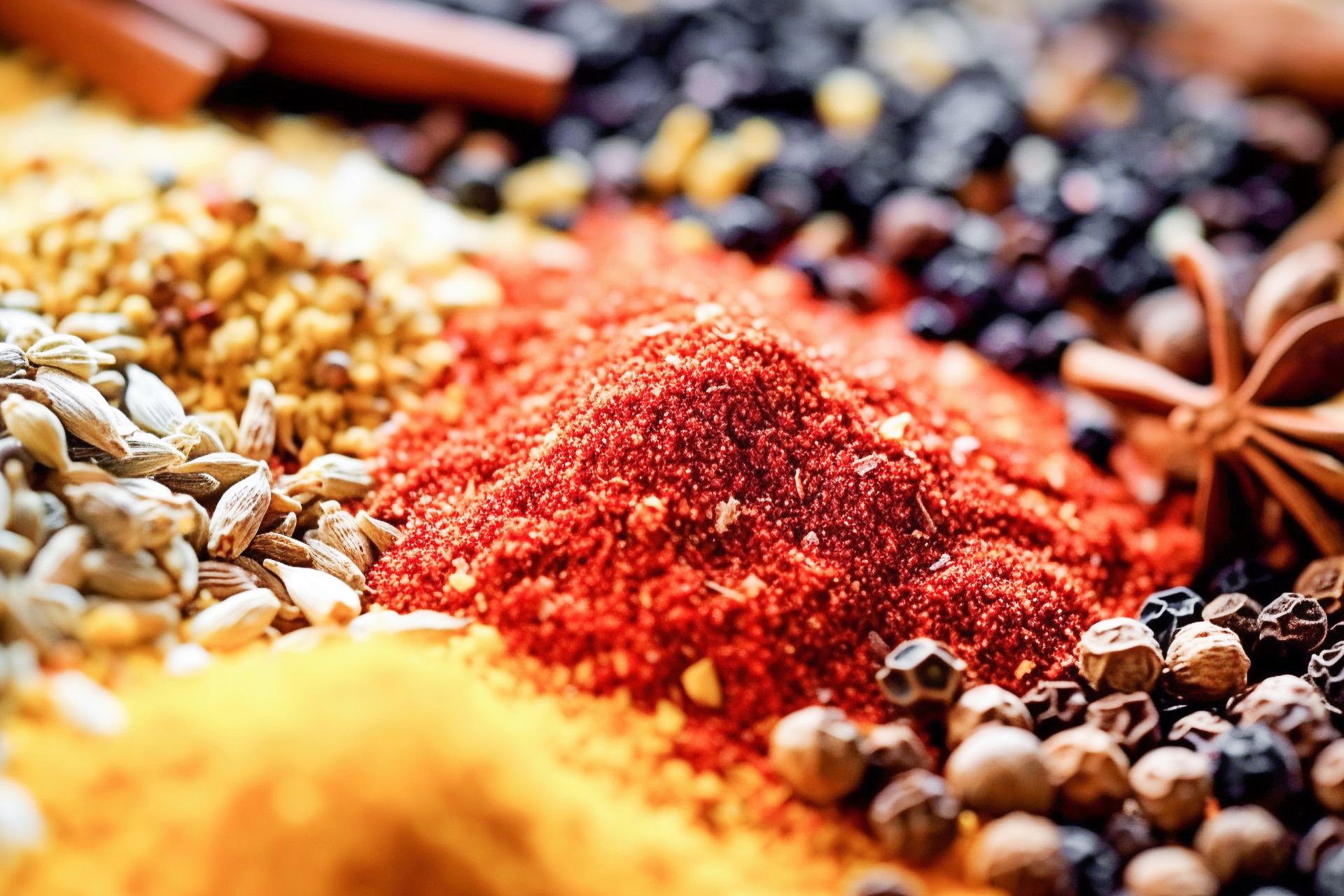 Spices spilling from jars: coriander seeds, cardamom, cinnamon sticks, chili peppers, and turmeric on a dark surface.