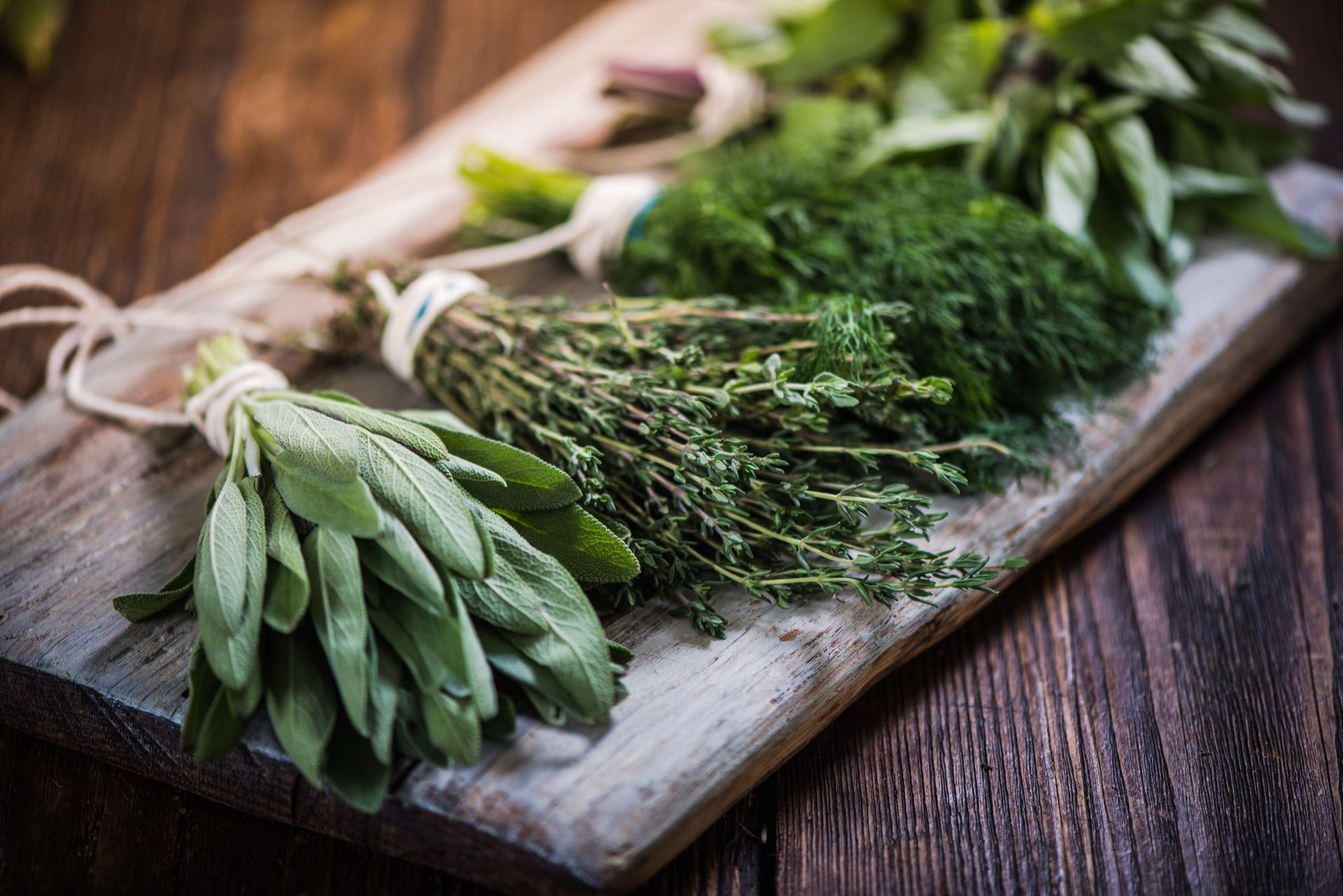 Bundles of fresh herbs on a wooden cutting board: sage, thyme, dill, basil.