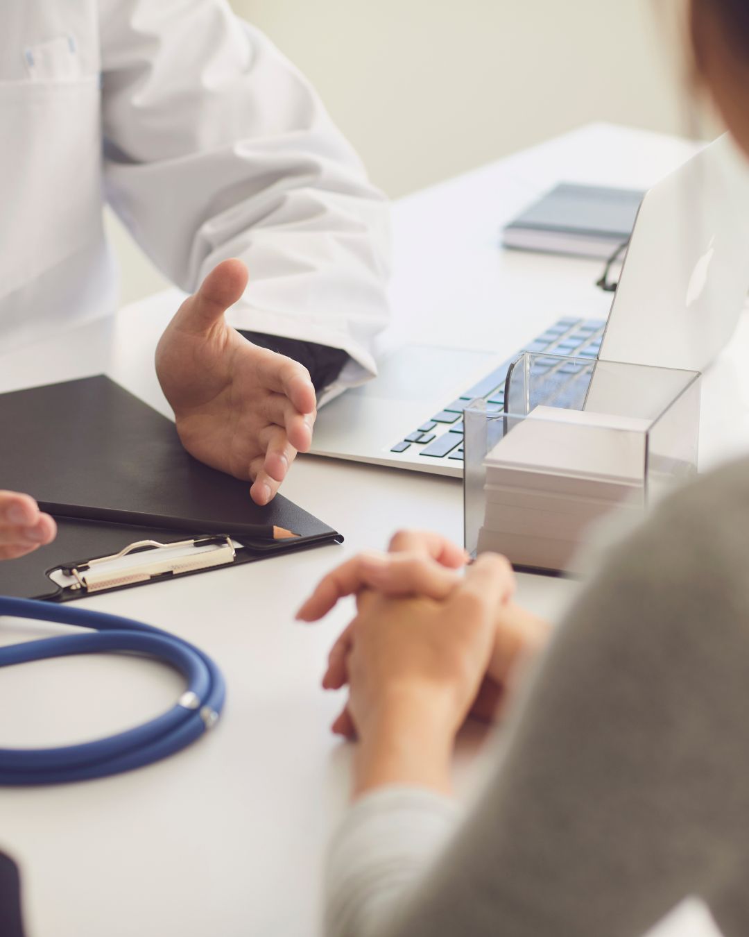 A doctor is talking to a patient who is sitting at a desk with a laptop.