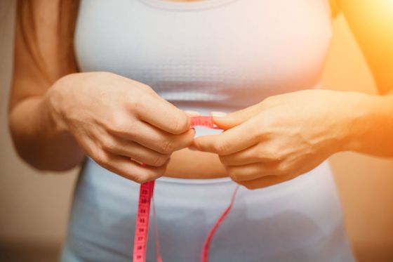Hands holding a pink measuring tape around a waist against a white top.