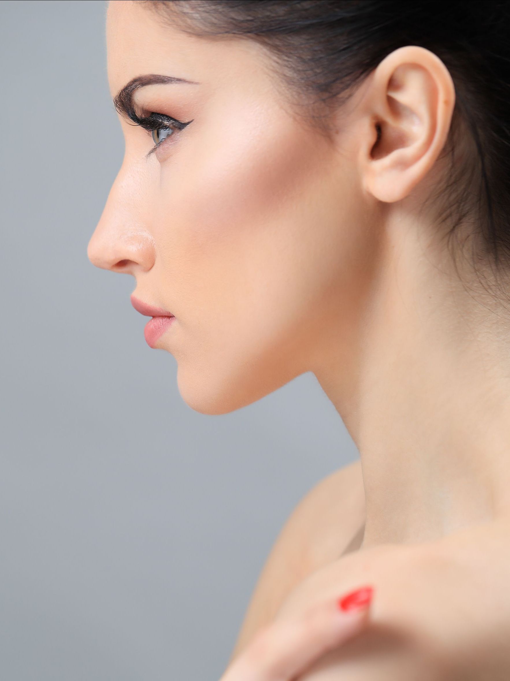 A close up of a woman 's face with red nails against a gray background.
