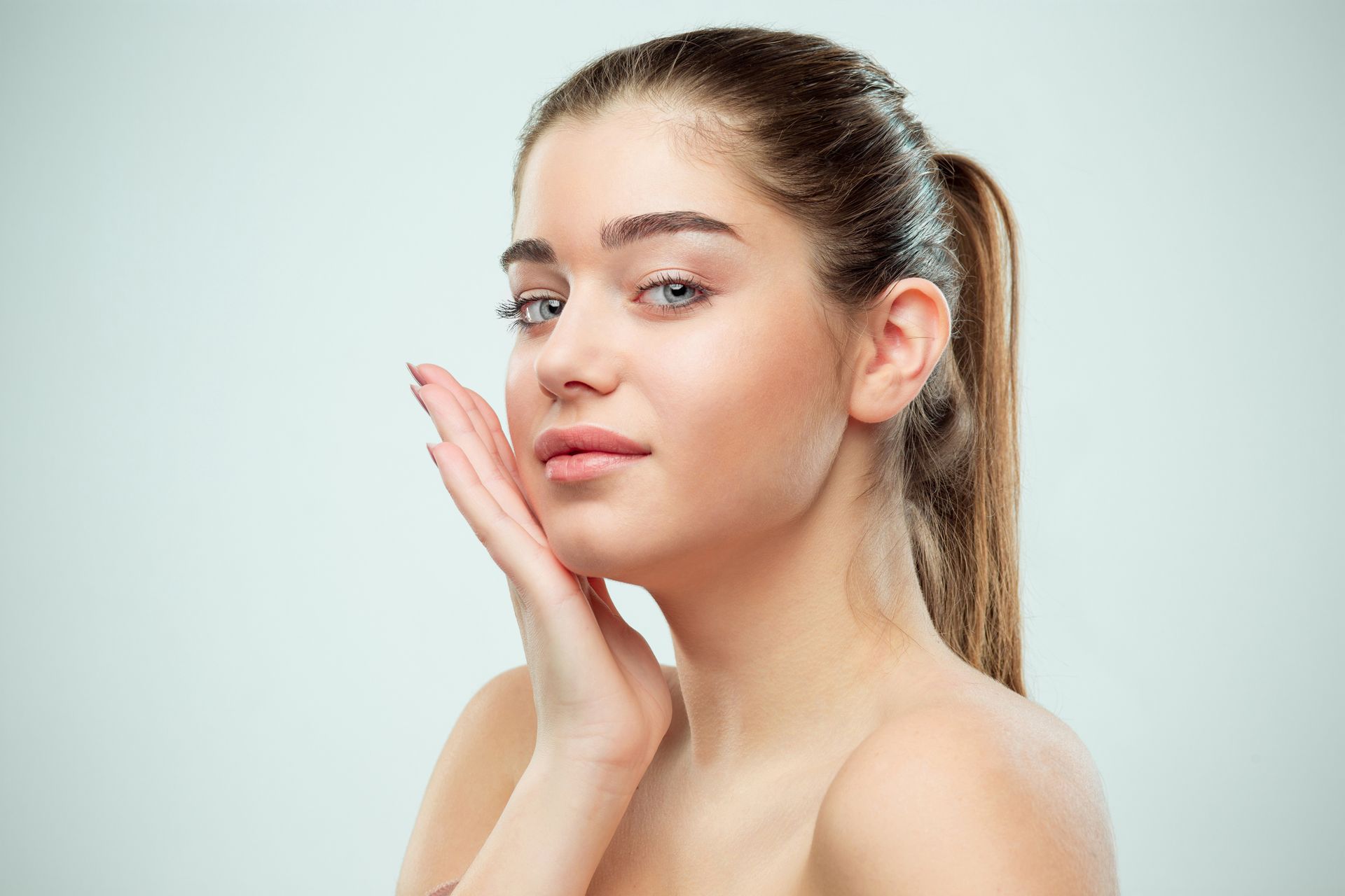 A woman is touching her face with her hand and looking at the camera.