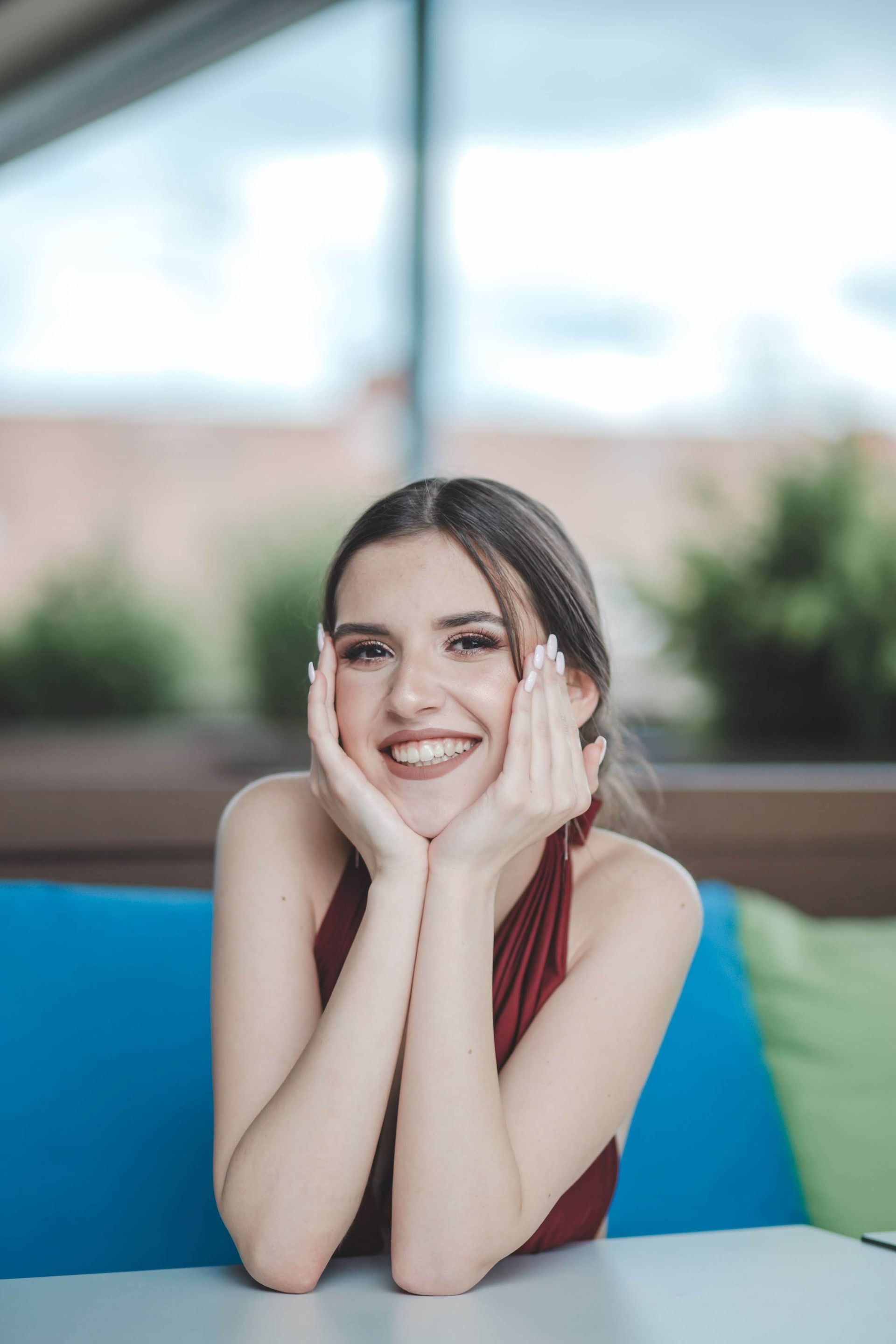 A woman is sitting at a table with her hands on her face and smiling.
