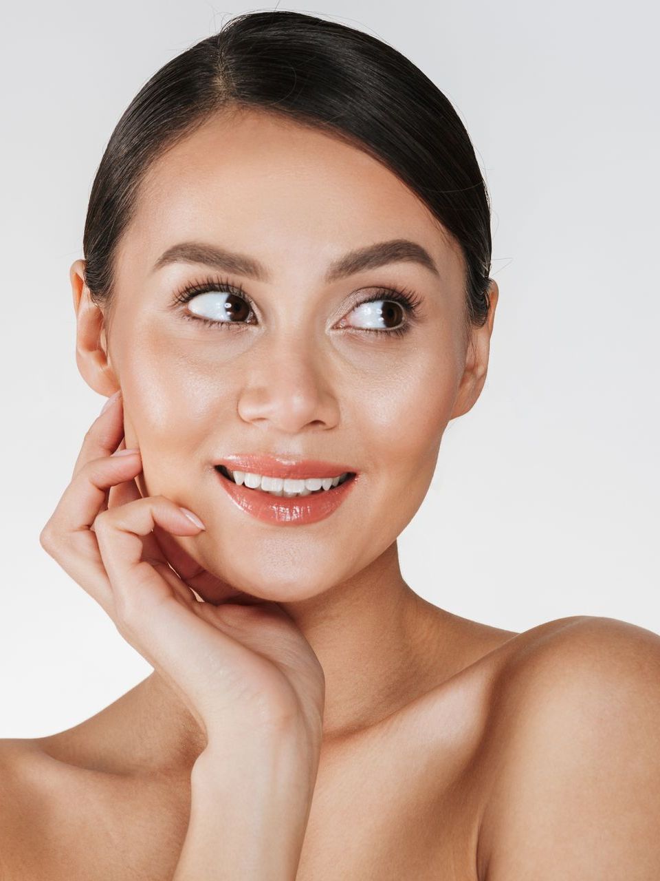 A woman is smiling and touching her face with her hand.