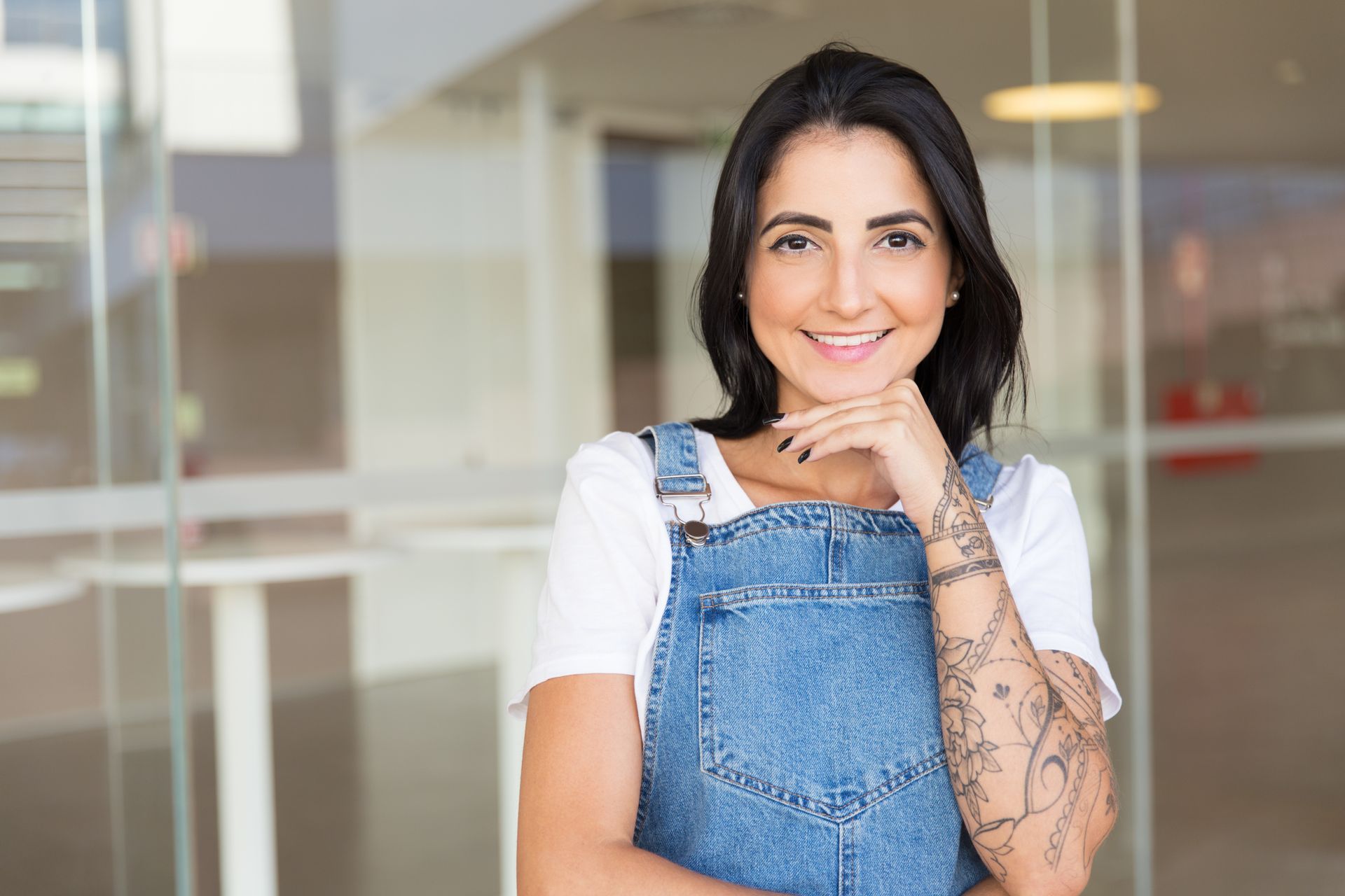 The woman is wearing overalls and has a tattoo on her arm.