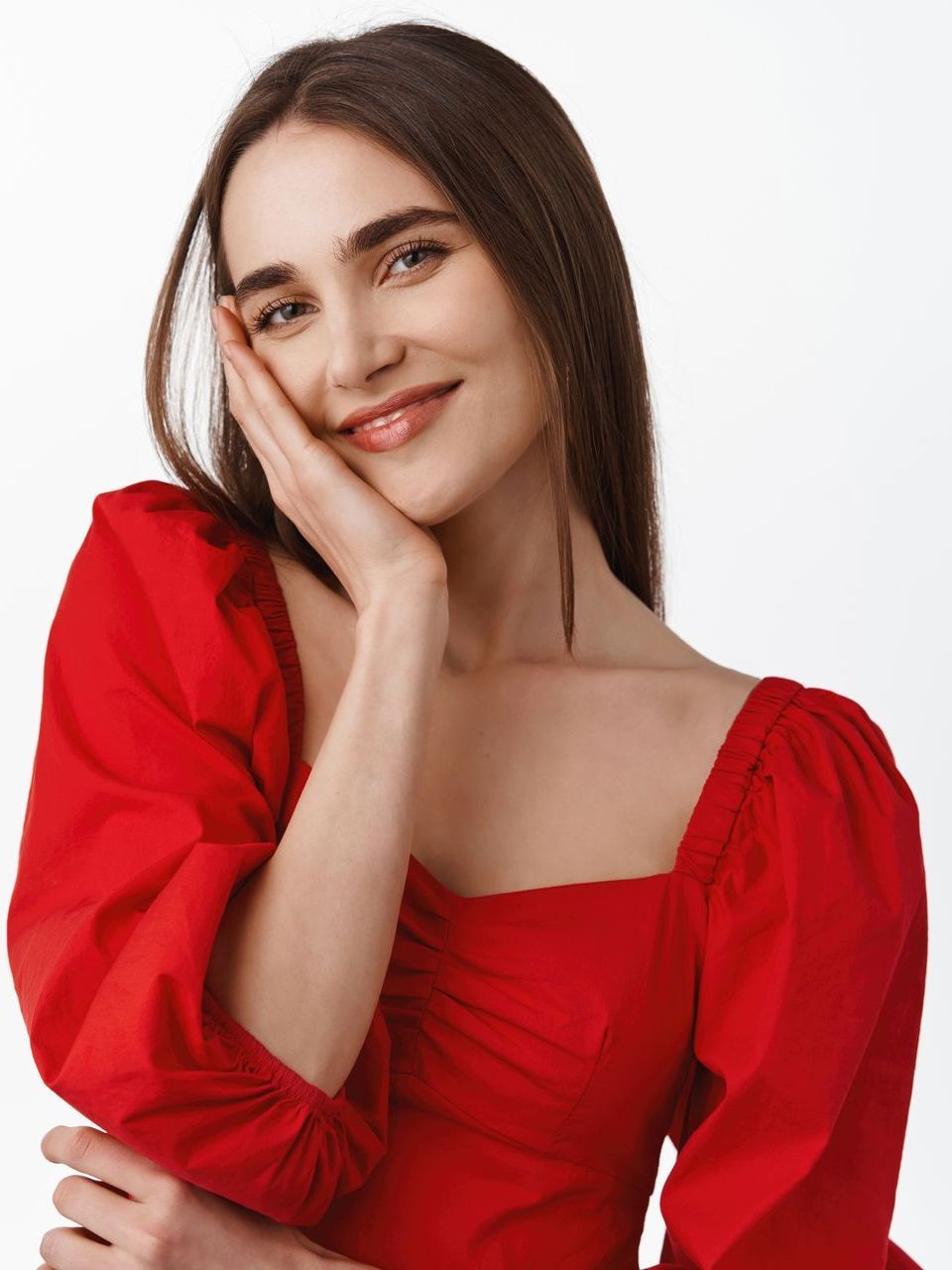 A woman in a red dress is smiling with her hand on her face.