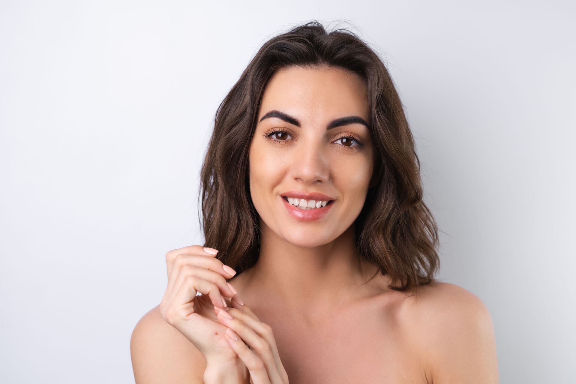 A woman without a shirt is smiling and touching her hair.