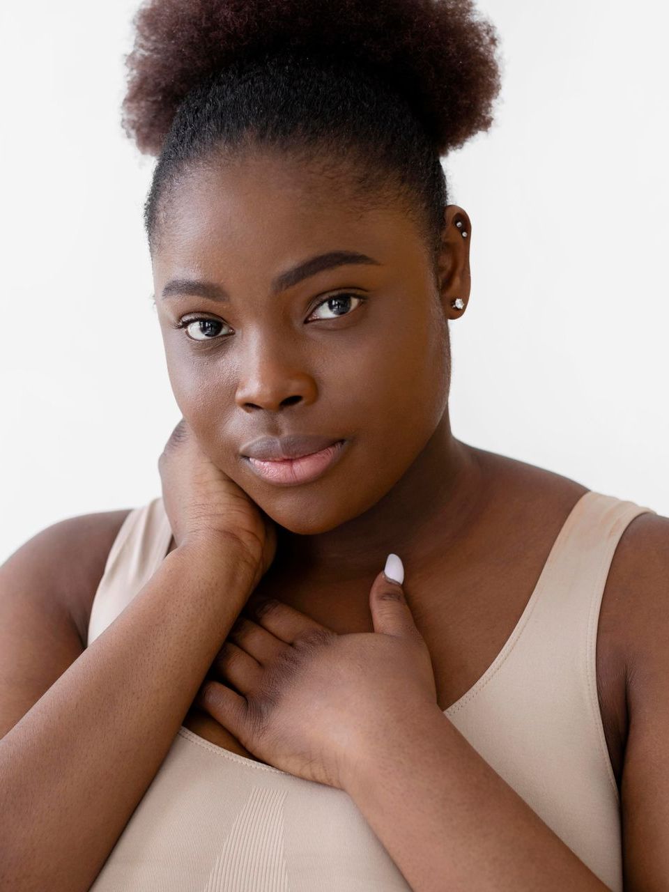 A woman in a tan tank top is holding her hand to her chest.