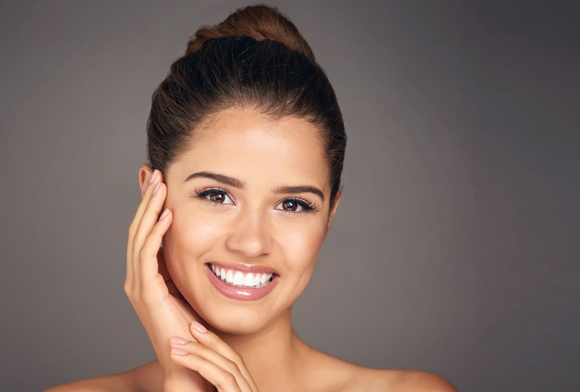 A woman is smiling and touching her face with her hand.