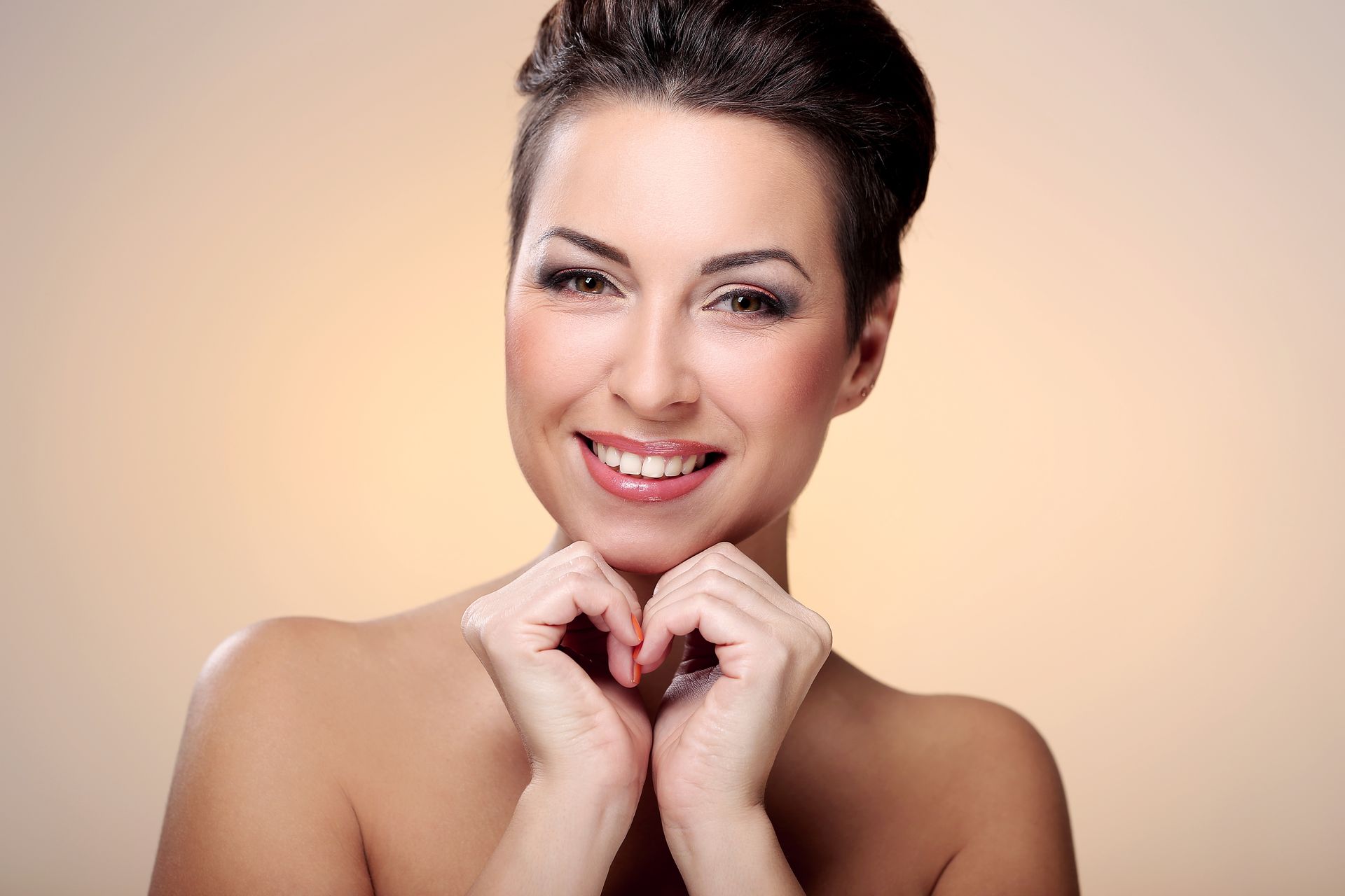 A woman is smiling and making a heart shape with her hands.