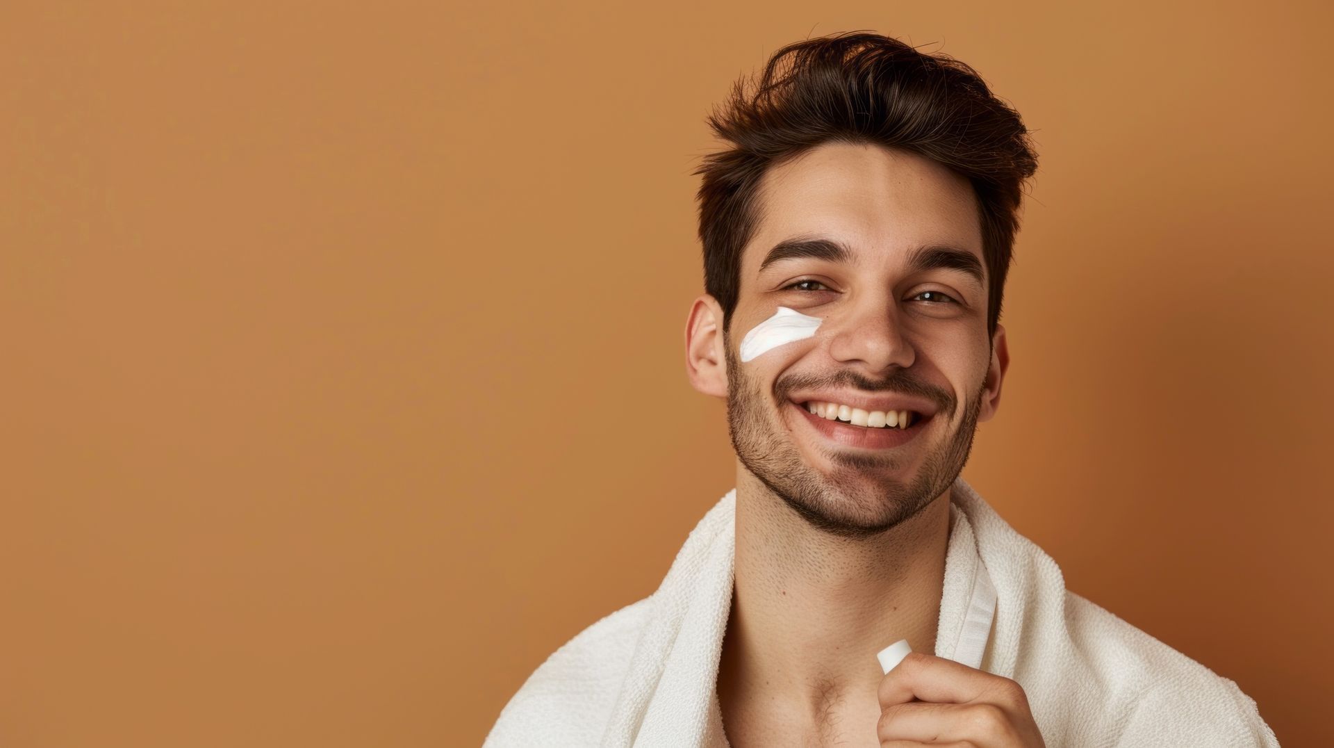 A man is smiling while applying cream to his face.
