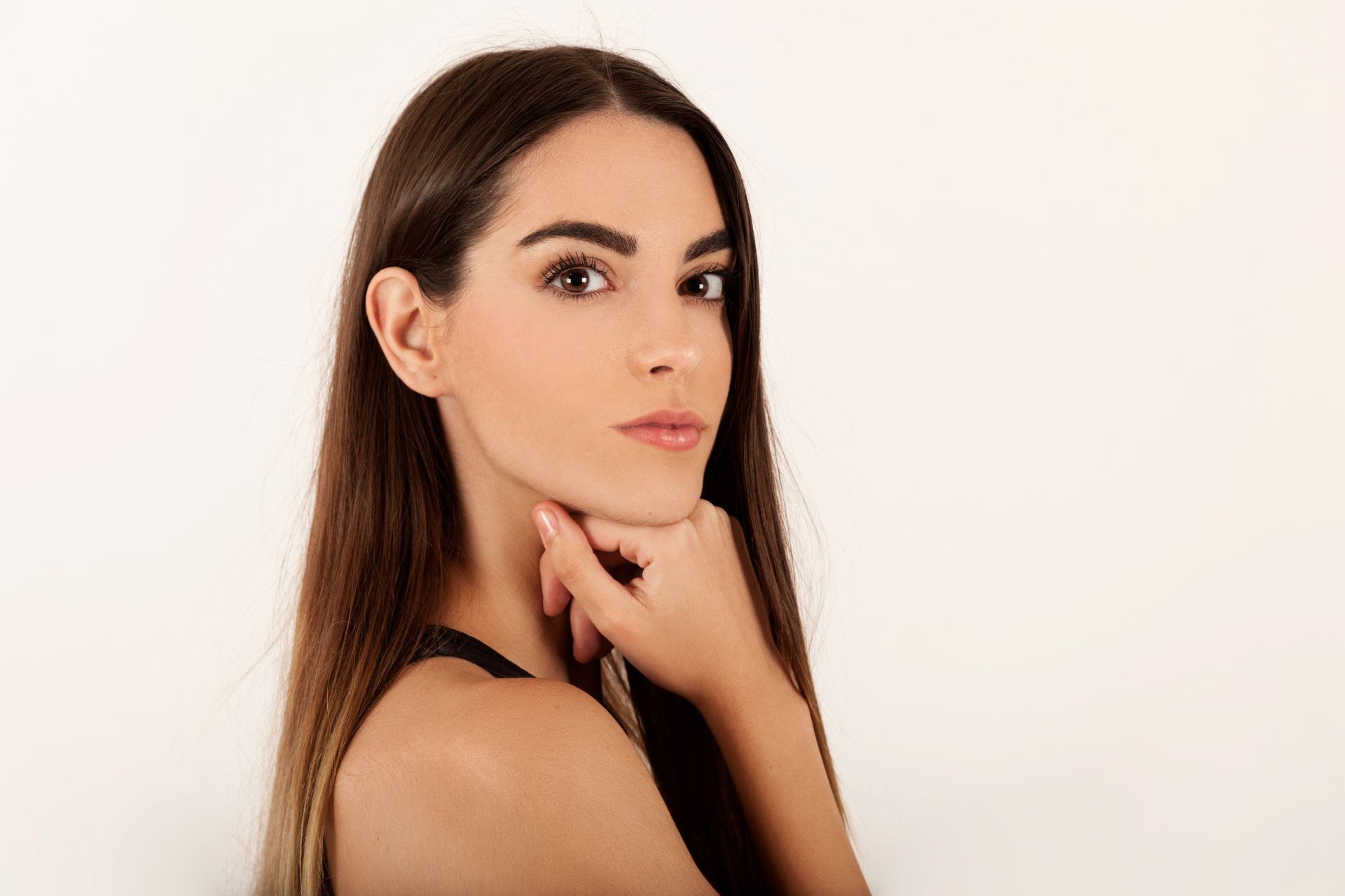 A woman with long hair is holding her hand to her chin and looking at the camera.