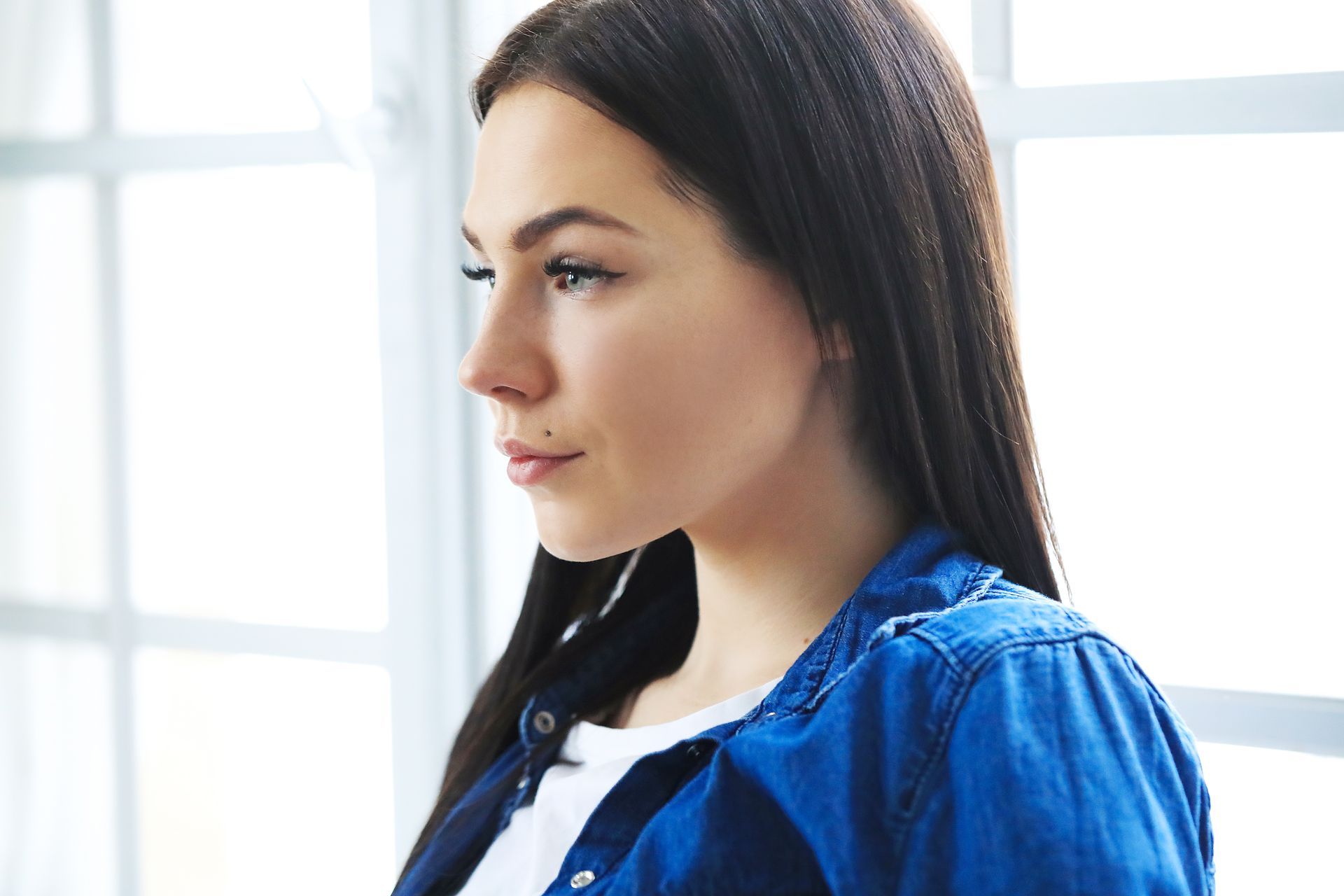 A woman in a blue shirt is looking out of a window.