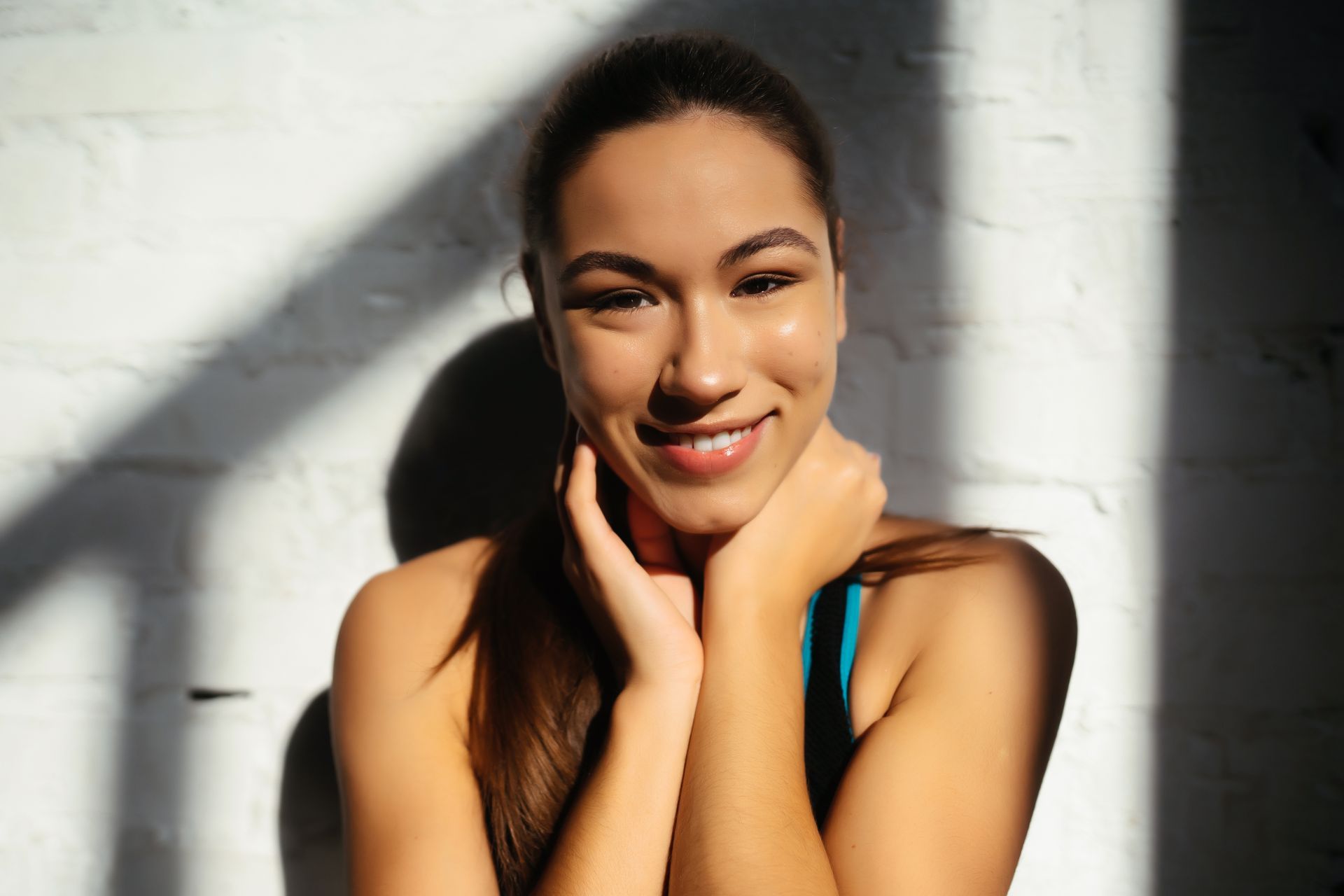 A woman is smiling while sitting in front of a white brick wall.