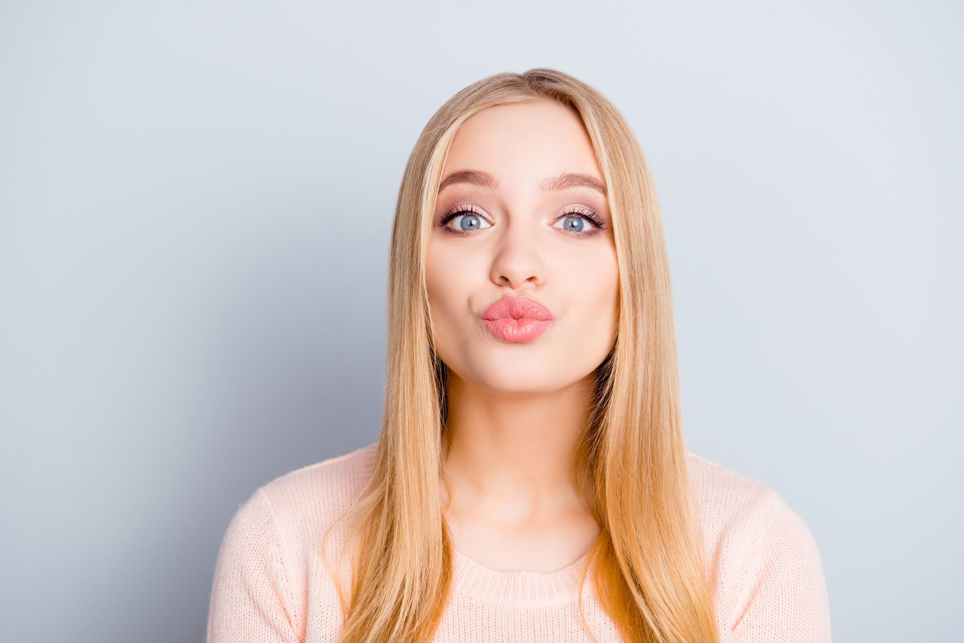 A woman in a pink sweater is blowing a kiss.