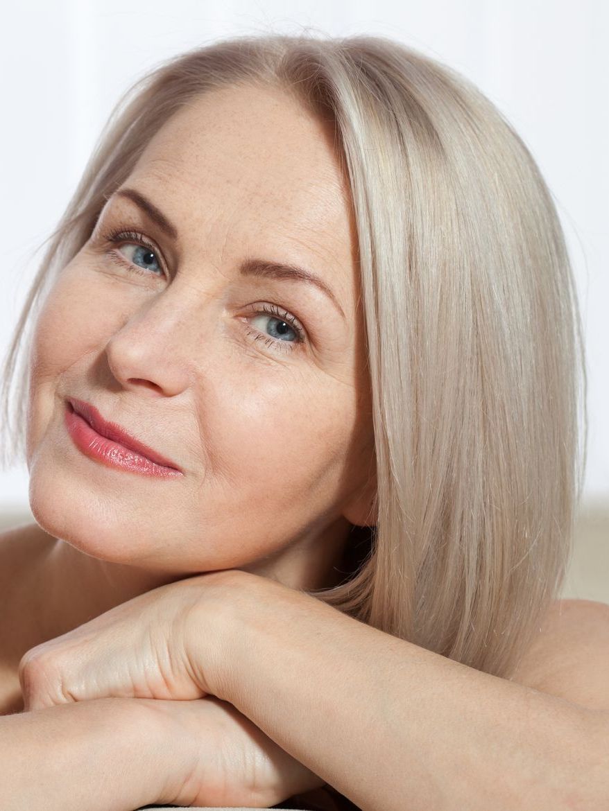 A woman with blonde hair is smiling with her hands on her face.