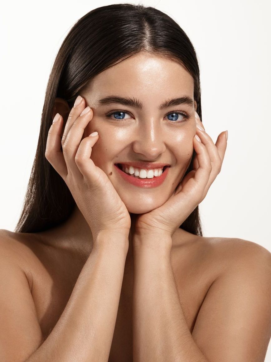A woman is smiling and touching her face with her hands.