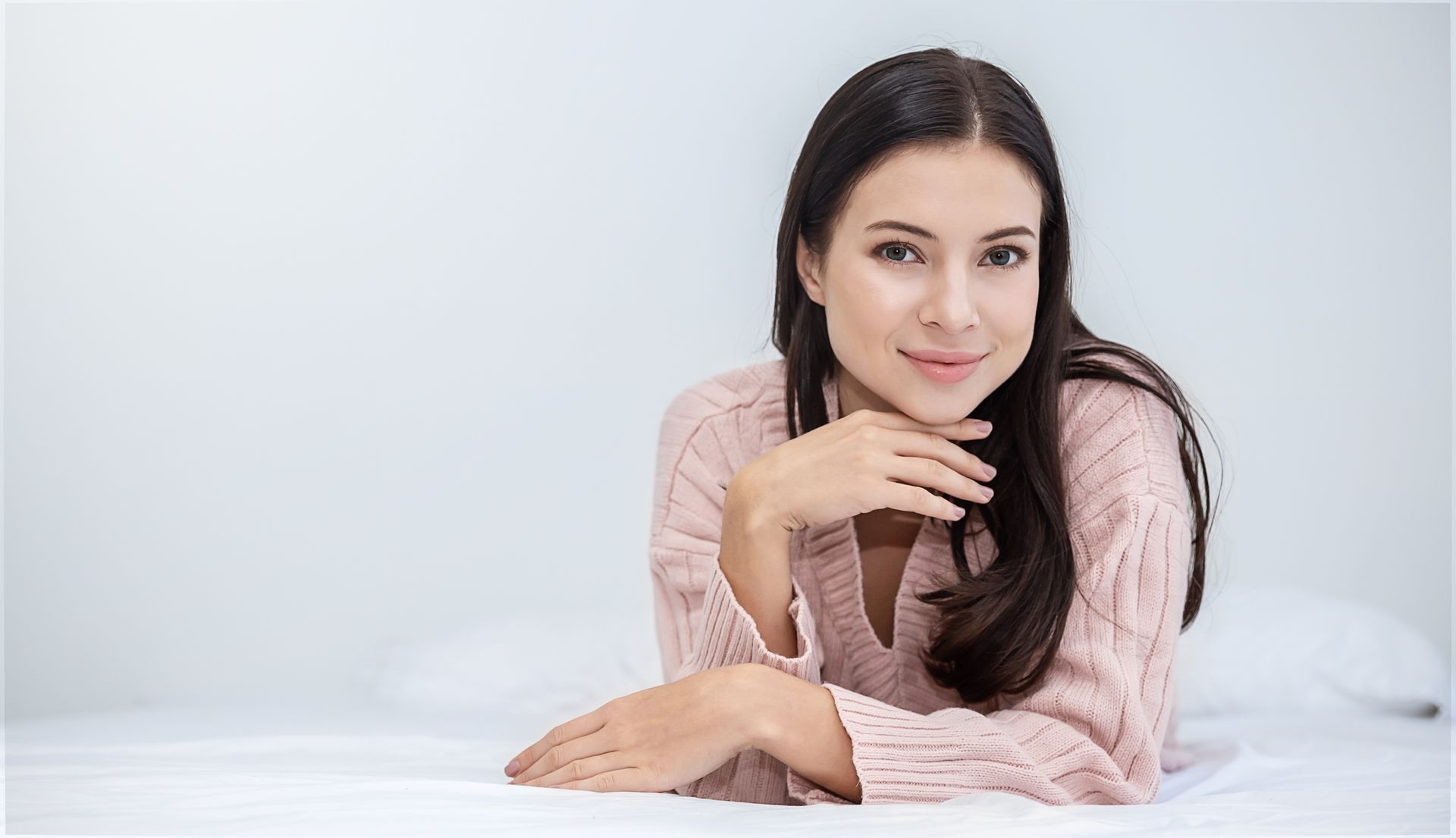 A woman in a pink sweater is laying on a bed.