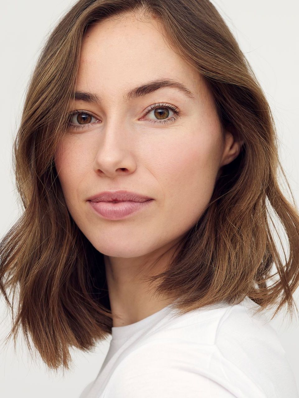 A woman with brown hair is wearing a white shirt and looking at the camera.