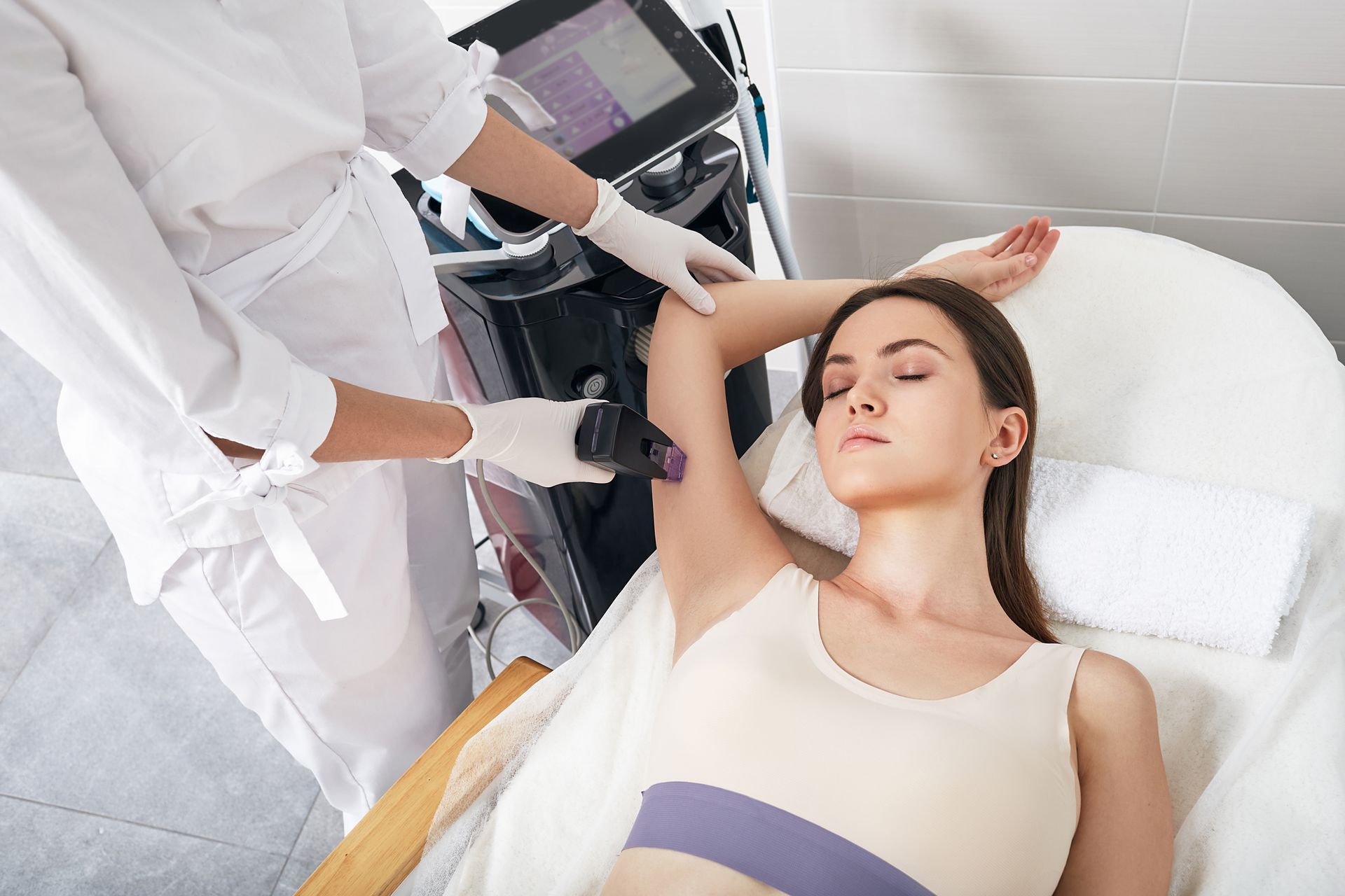 Technician performing laser treatment on a patient lying on a clinic bed