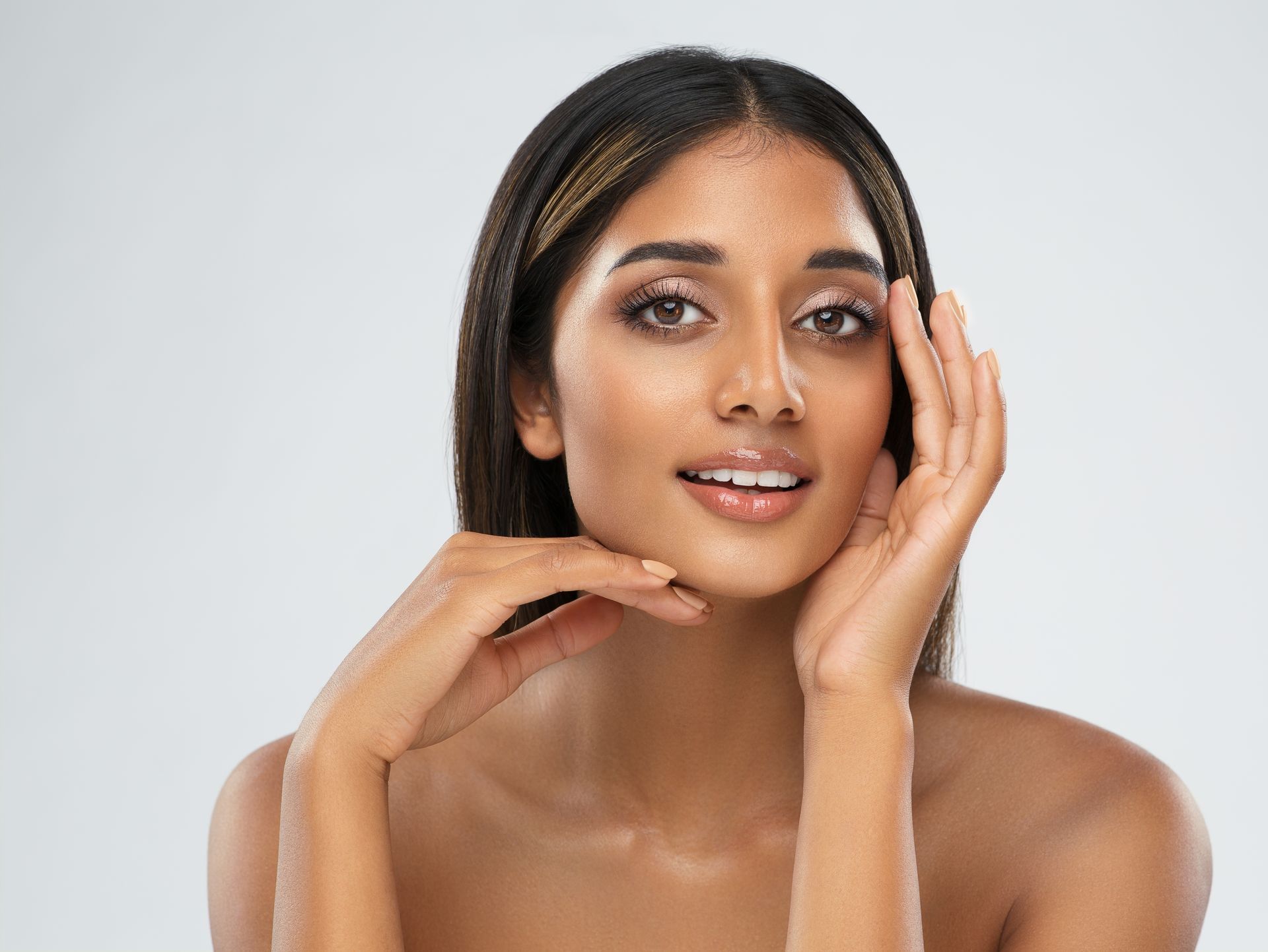 A woman is touching her face with her hands and smiling.