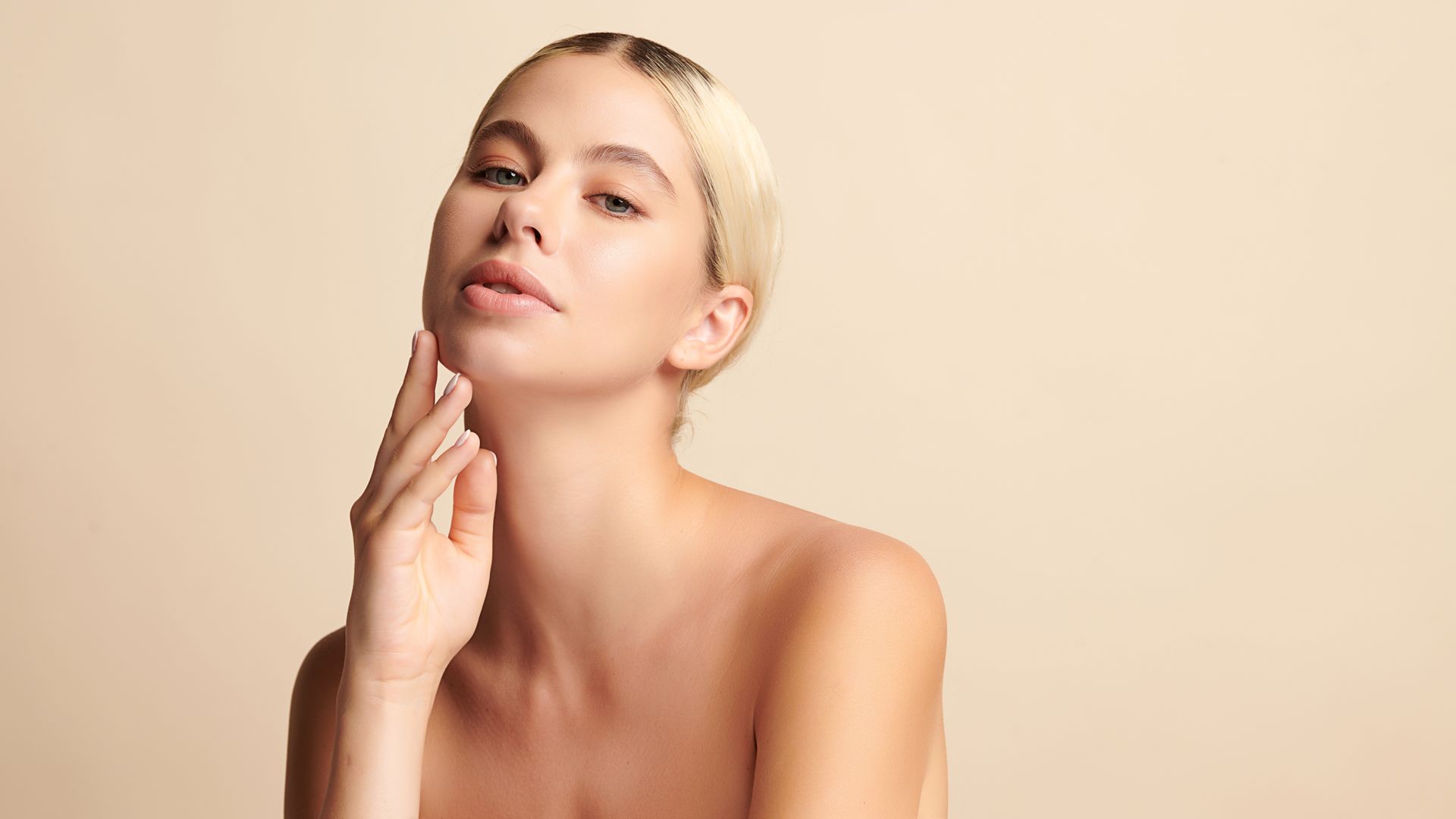 A woman is touching her face with her hand and looking at the camera.