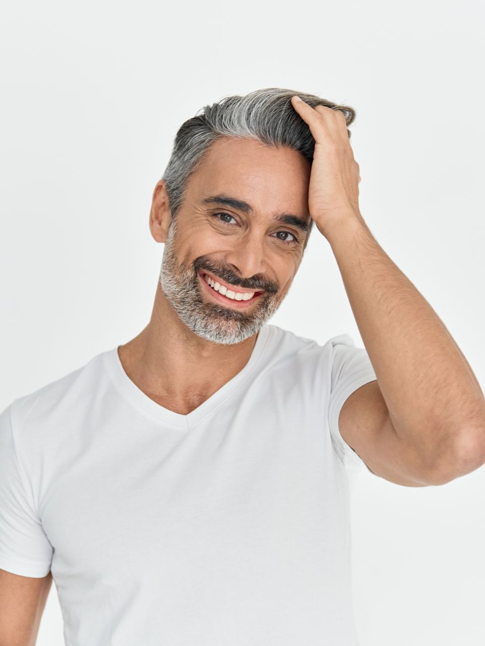 Smiling man in a white T-shirt running his hand through gray hair against a white background