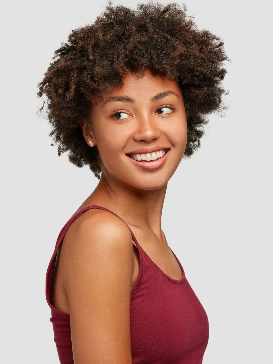 A woman with curly hair is smiling and wearing a red tank top