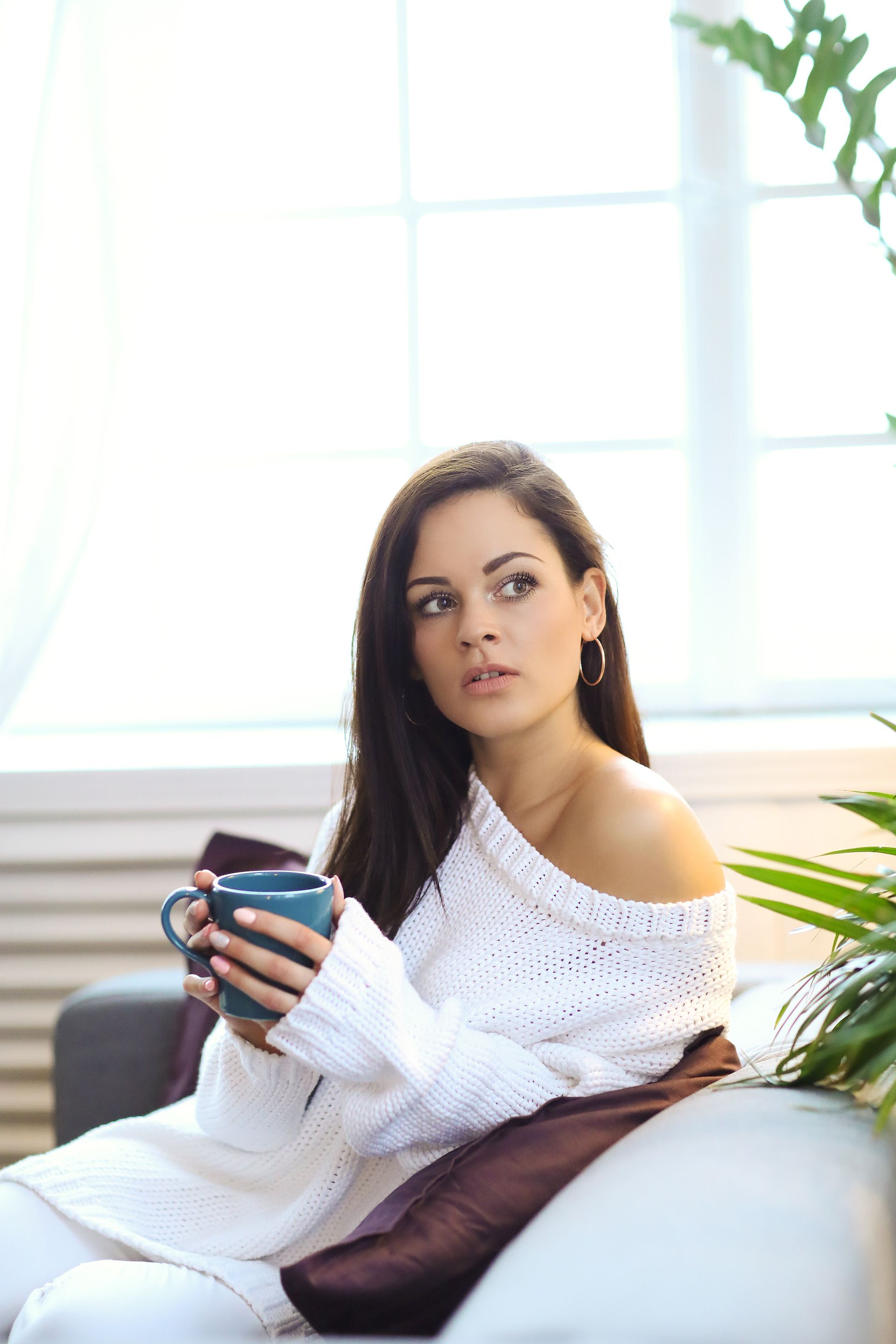 A woman is sitting on a couch holding a cup of coffee.