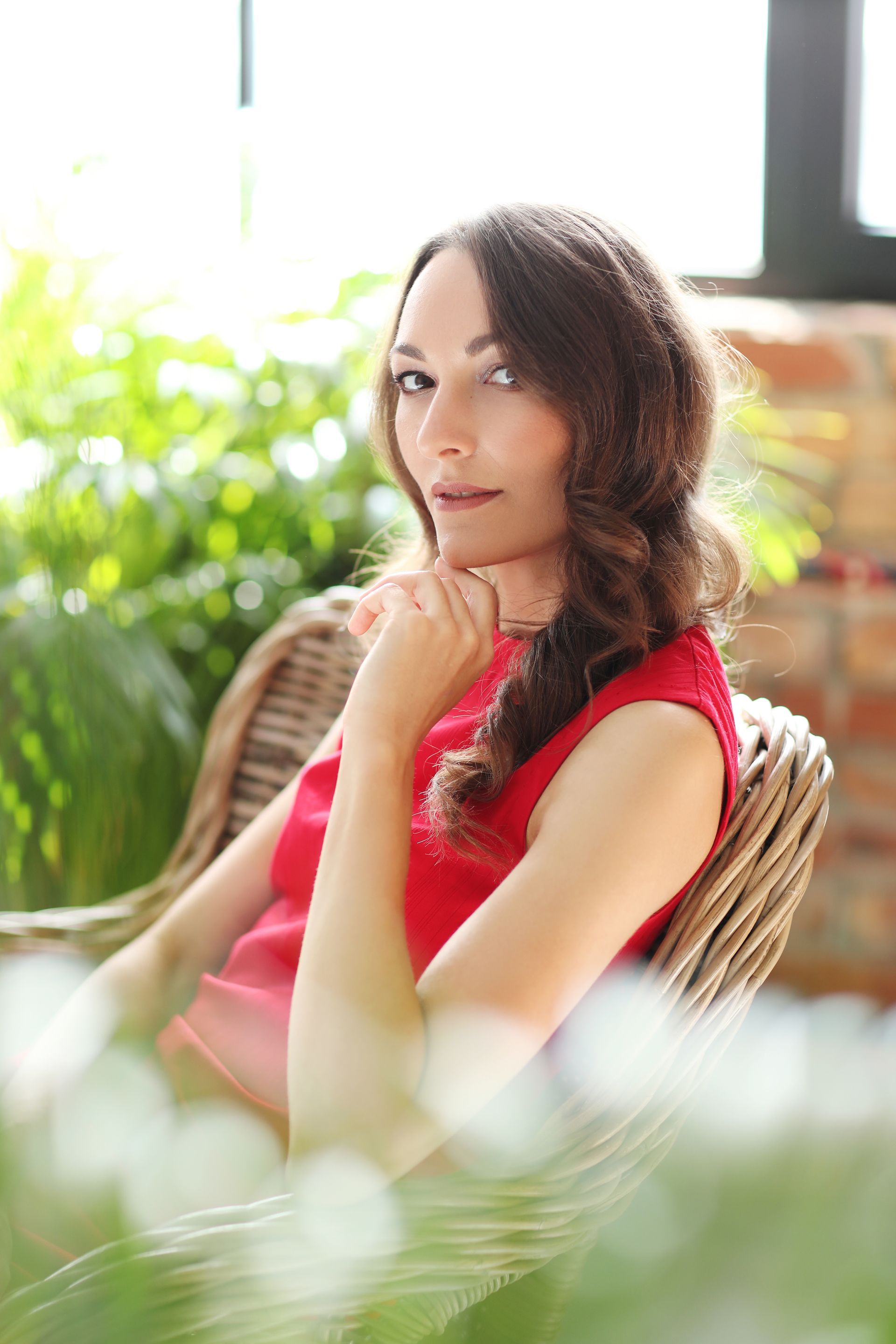 A woman in a red dress is sitting in a wicker chair.