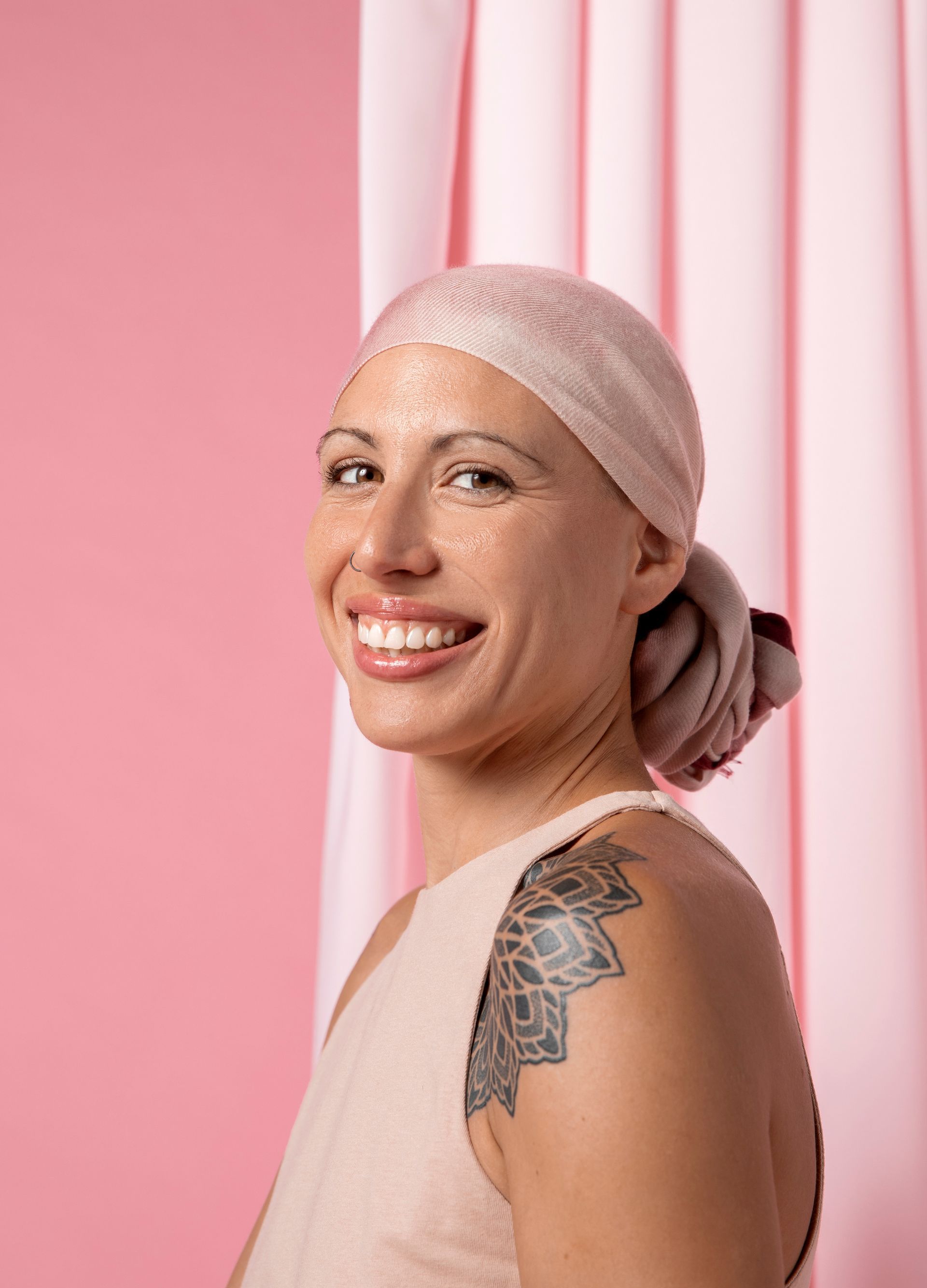 A woman with a scarf on her head and a tattoo on her shoulder is smiling.