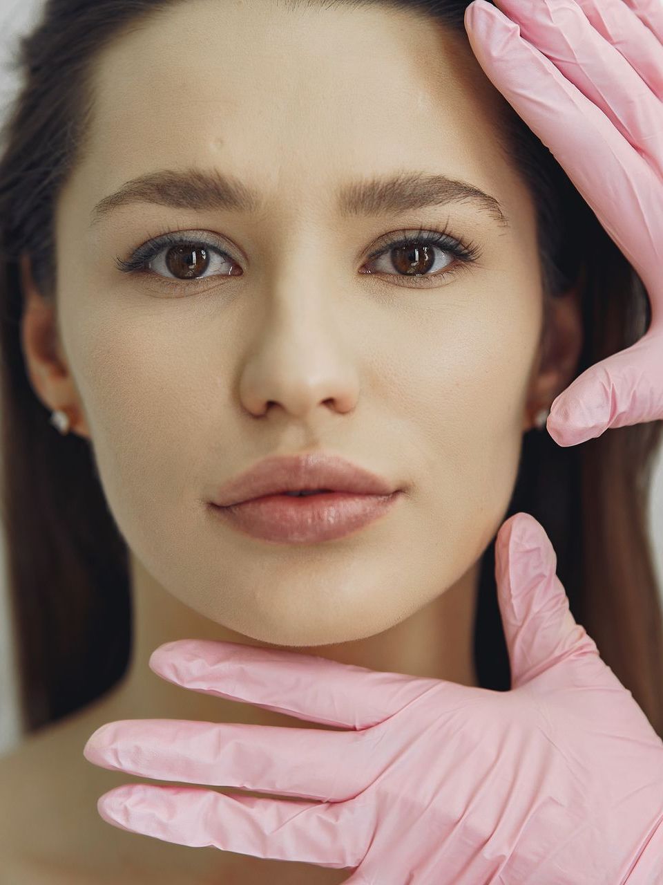 A woman wearing pink gloves is looking at her face.