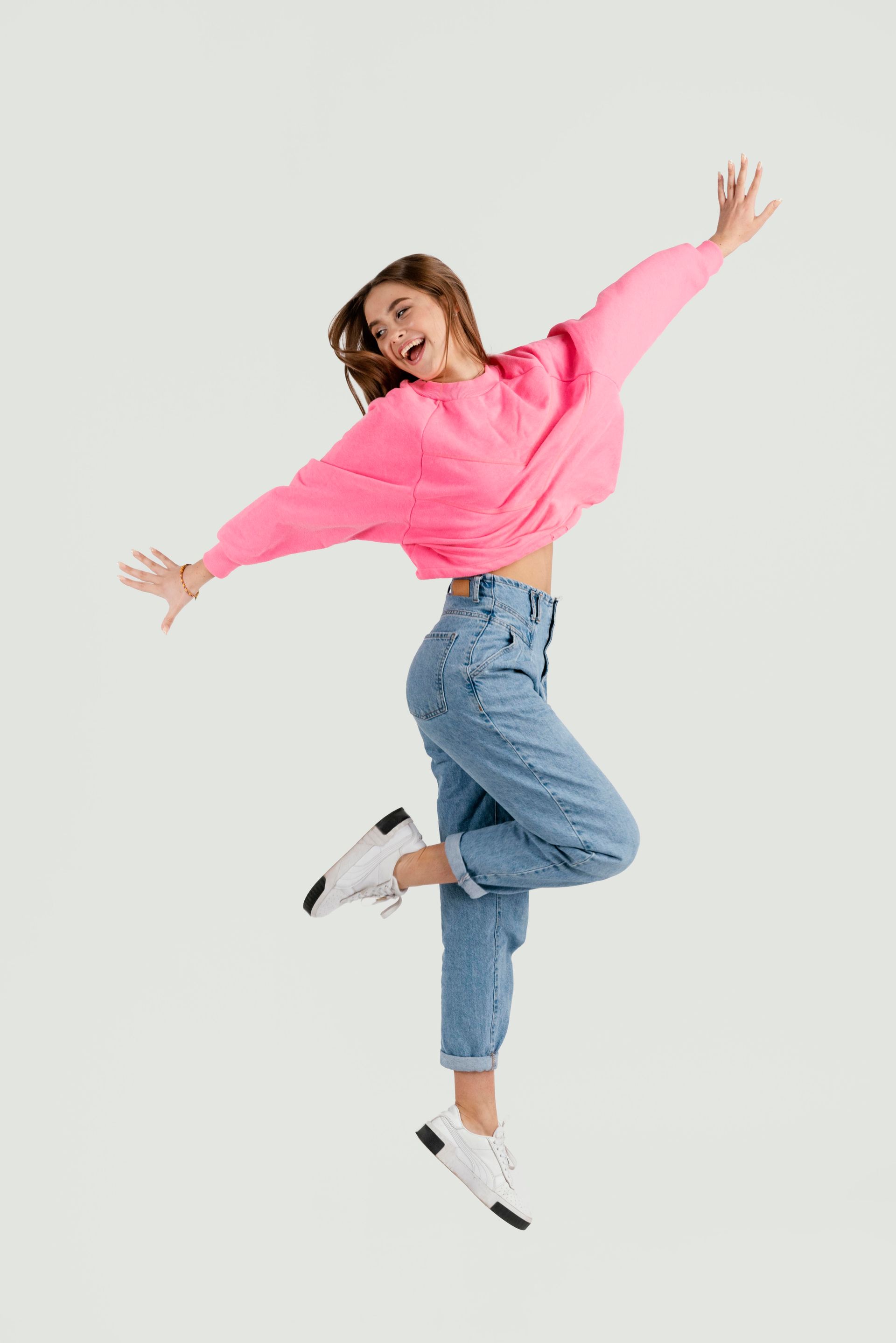 A woman in a pink sweater and blue jeans is jumping in the air.