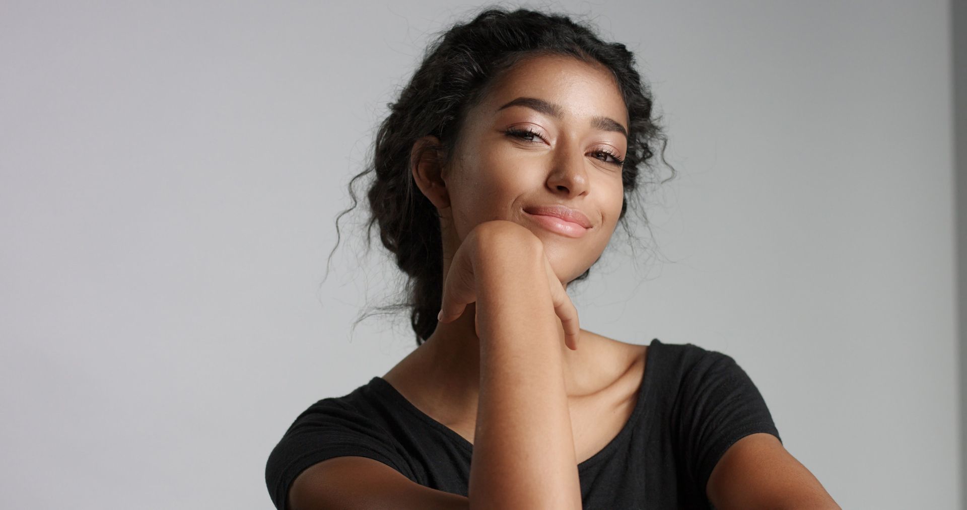 A young woman is smiling with her hand on her chin.