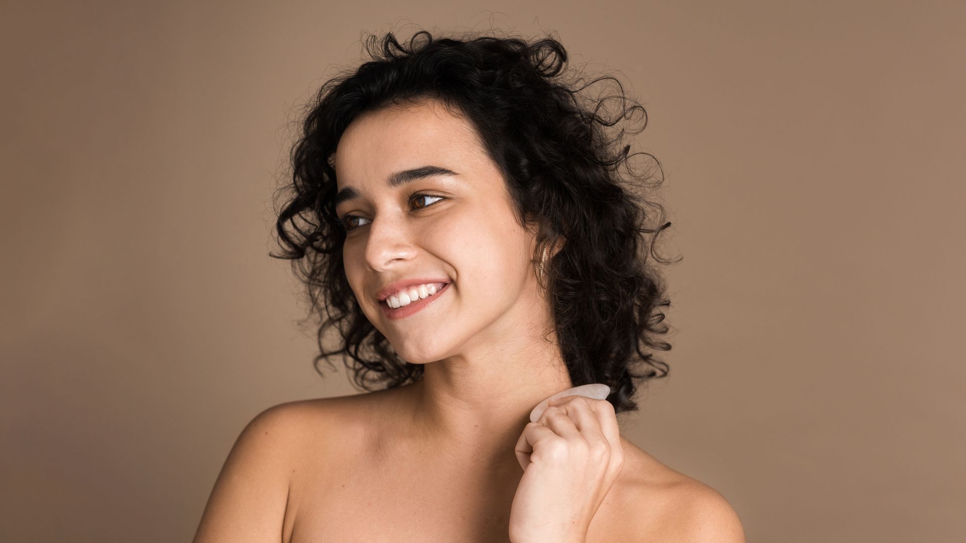 A woman with curly hair is smiling and holding a bottle of perfume.