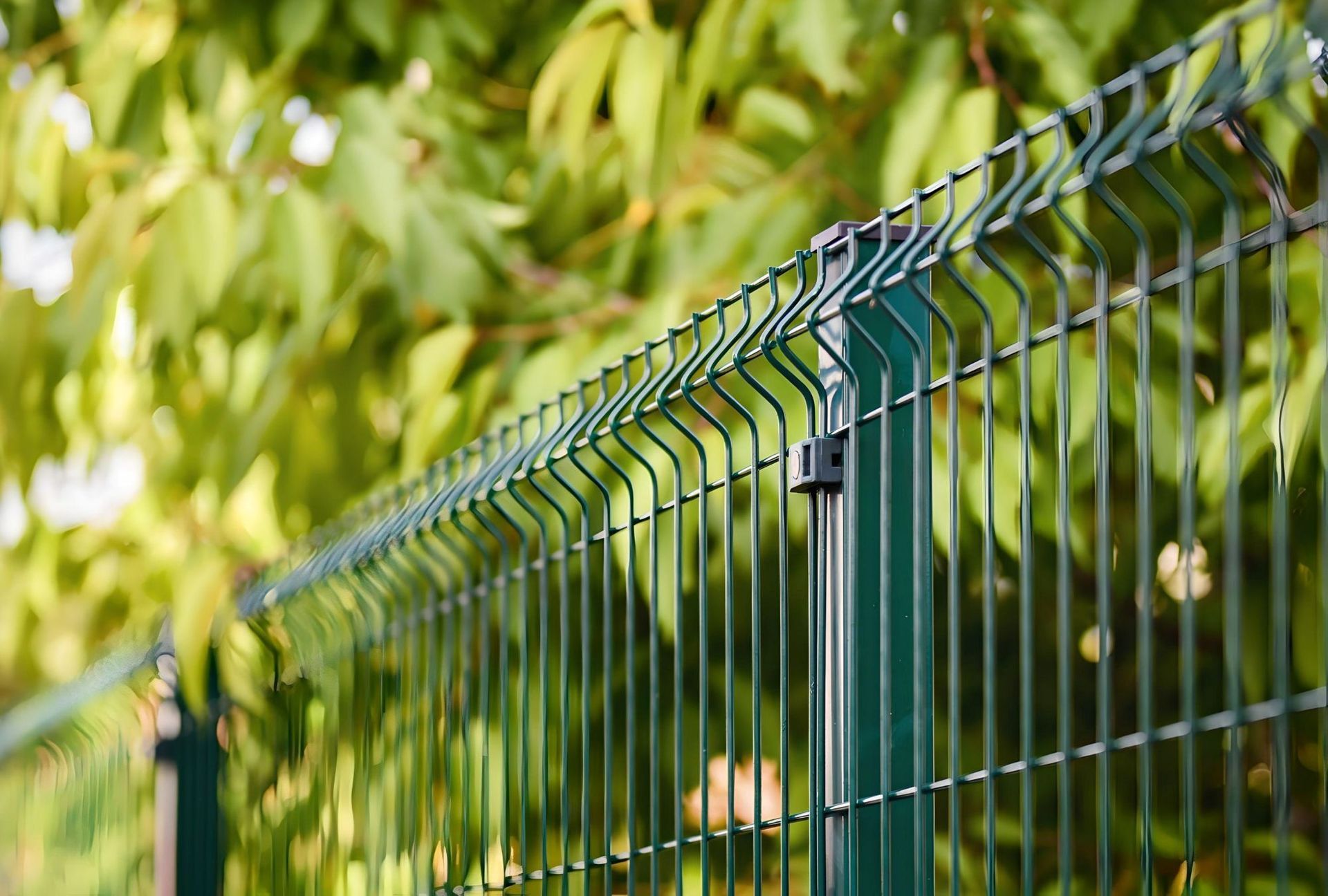 Metal fence with green foliage in the background and sunlight filtering through.