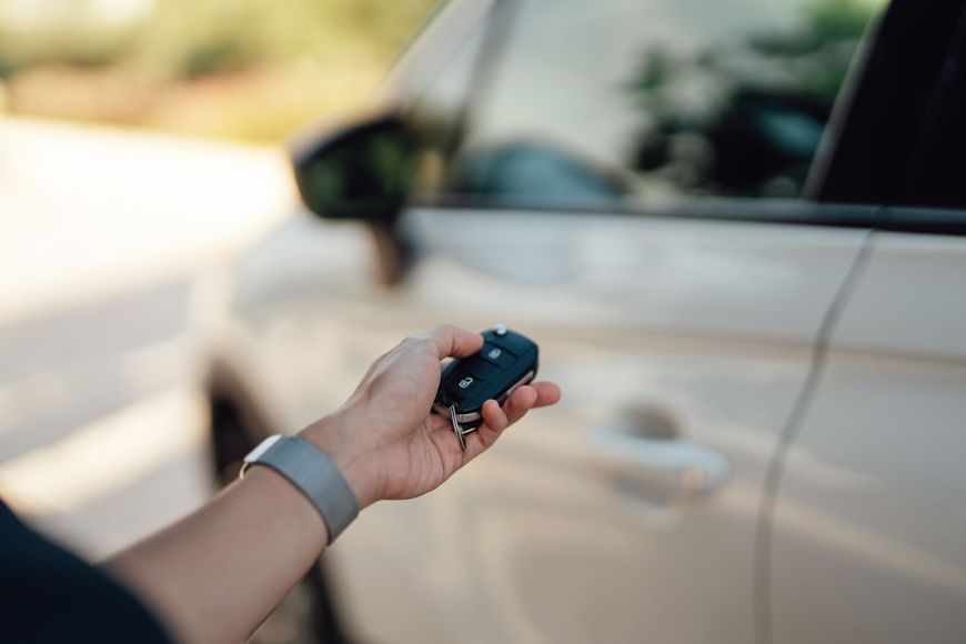Mano che tiene le chiavi di un'auto, mentre apre la portiera bianca di un'auto all'aperto.