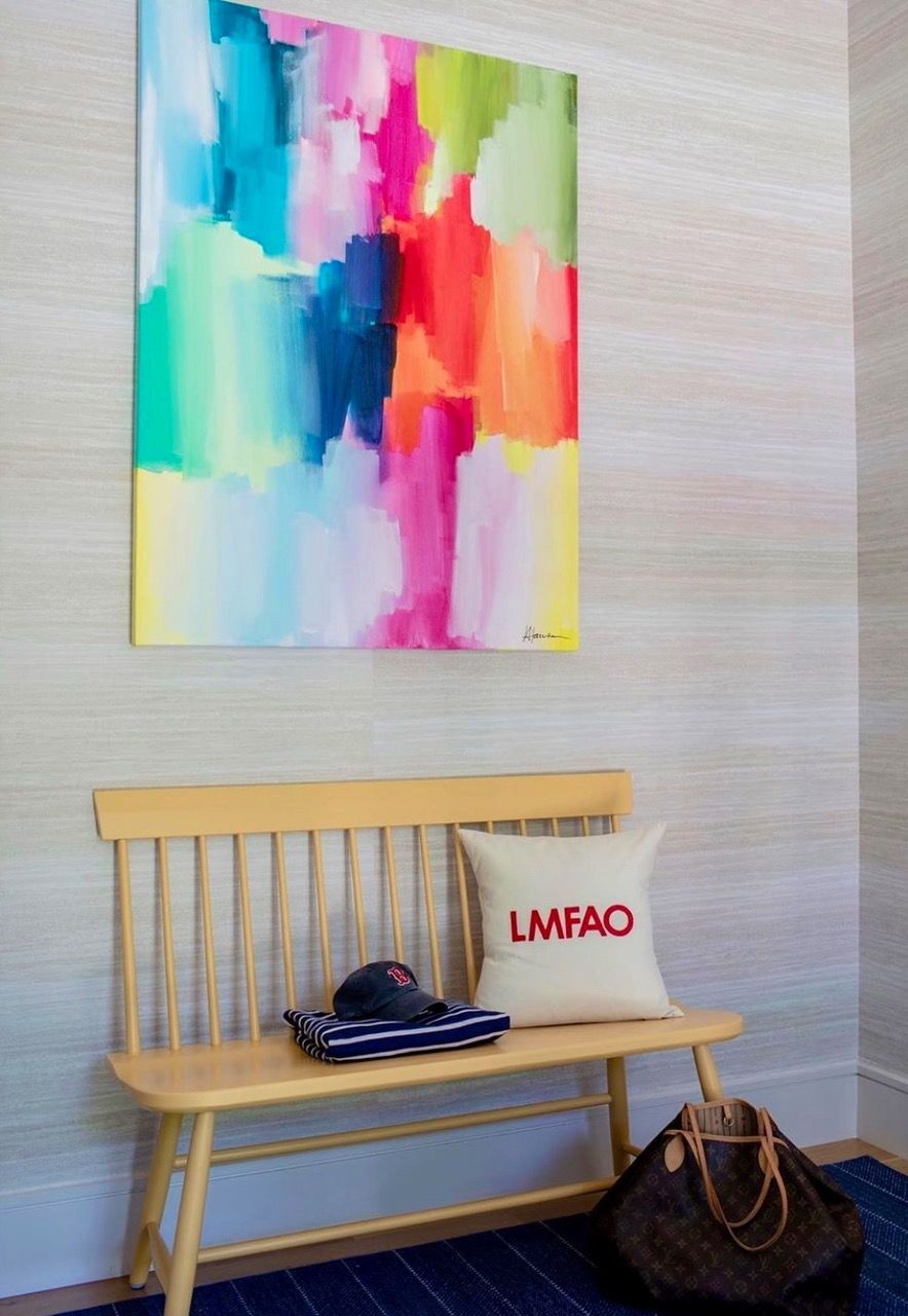 A wooden bench with a pillow and a painting on the wall above it.