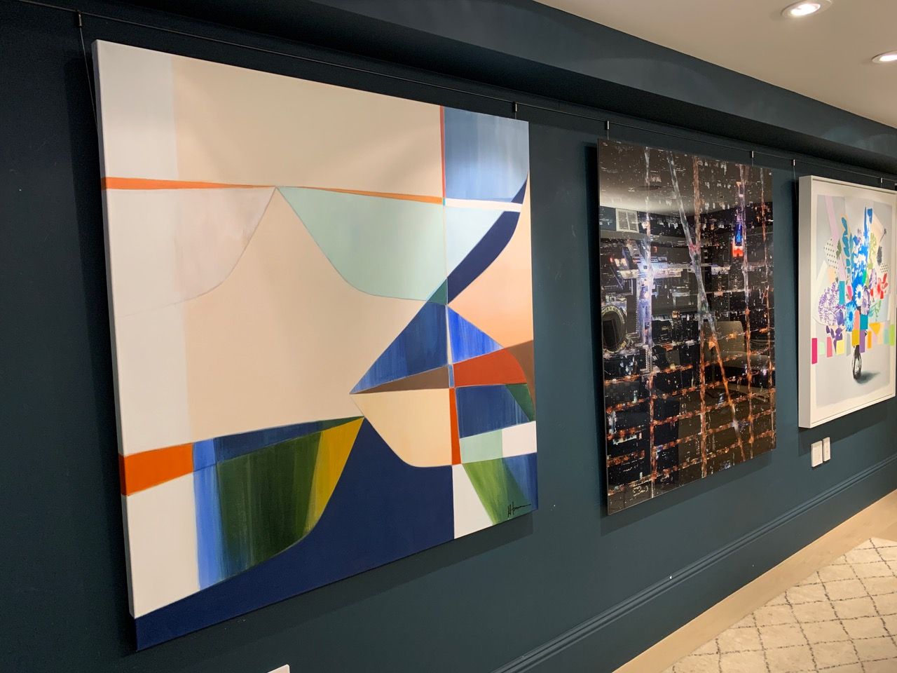 Three paintings are hanging on a wall in a hallway.