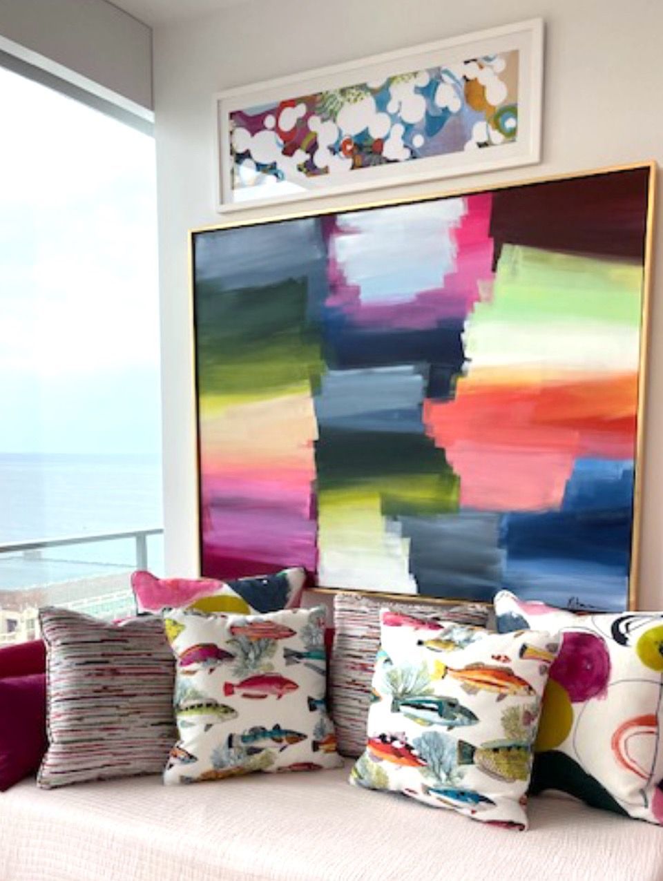 A colorful painting hangs above a couch with pillows