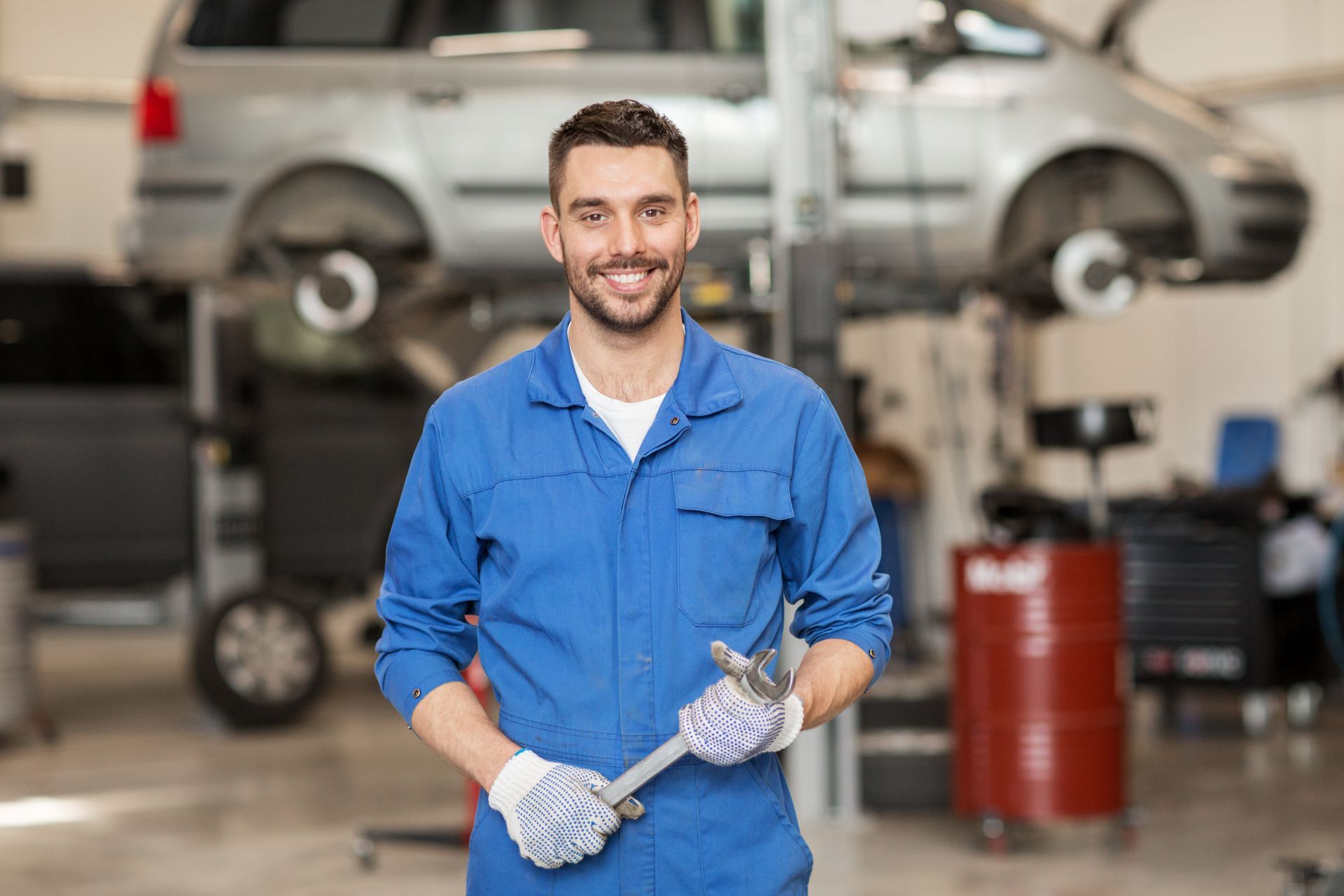 Mechanic in blue coveralls holding a wrench in an auto repair shop with a lifted car.