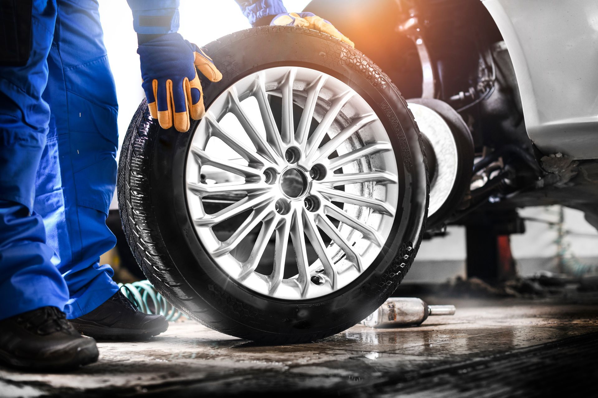 Mechanic working on a car wheel in a garage, with a silver alloy rim and tools on the wet floor