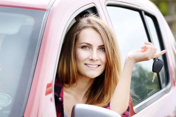 A woman driver emerges from her car window, holding the car key