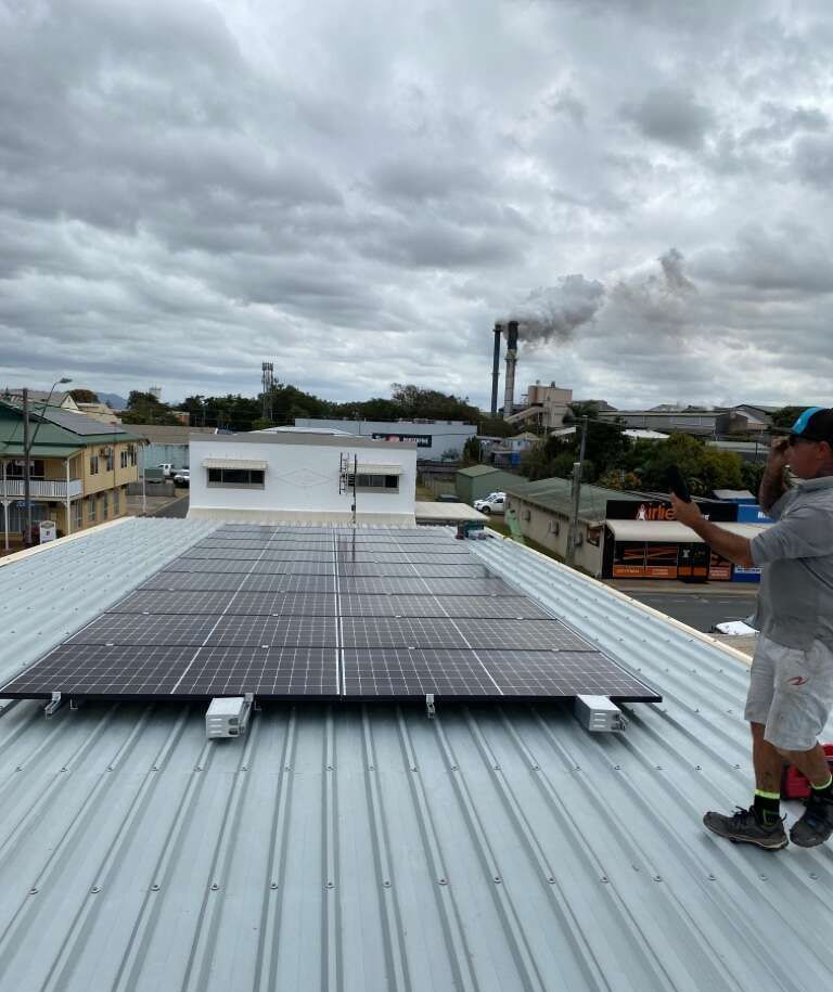 A Man Is Standing On Top Of A Roof With Solar Panels On It — Solar Power Whitsunday In Proserpine, QLD