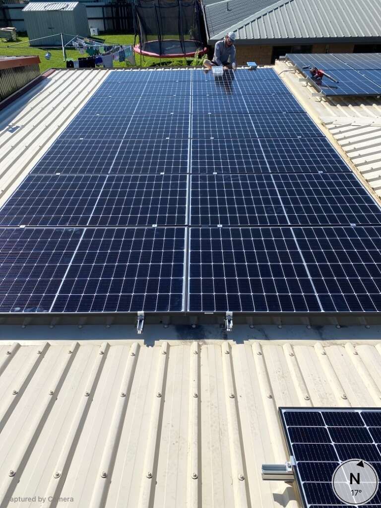 A Man Is Standing On Top Of A Roof With Solar Panels On It — Solar Power Whitsunday In Cannon Valley, QLD