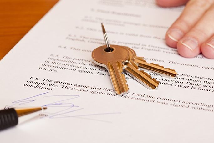 Keys resting on a document with a pen and a hand nearby, suggesting a signed agreement.