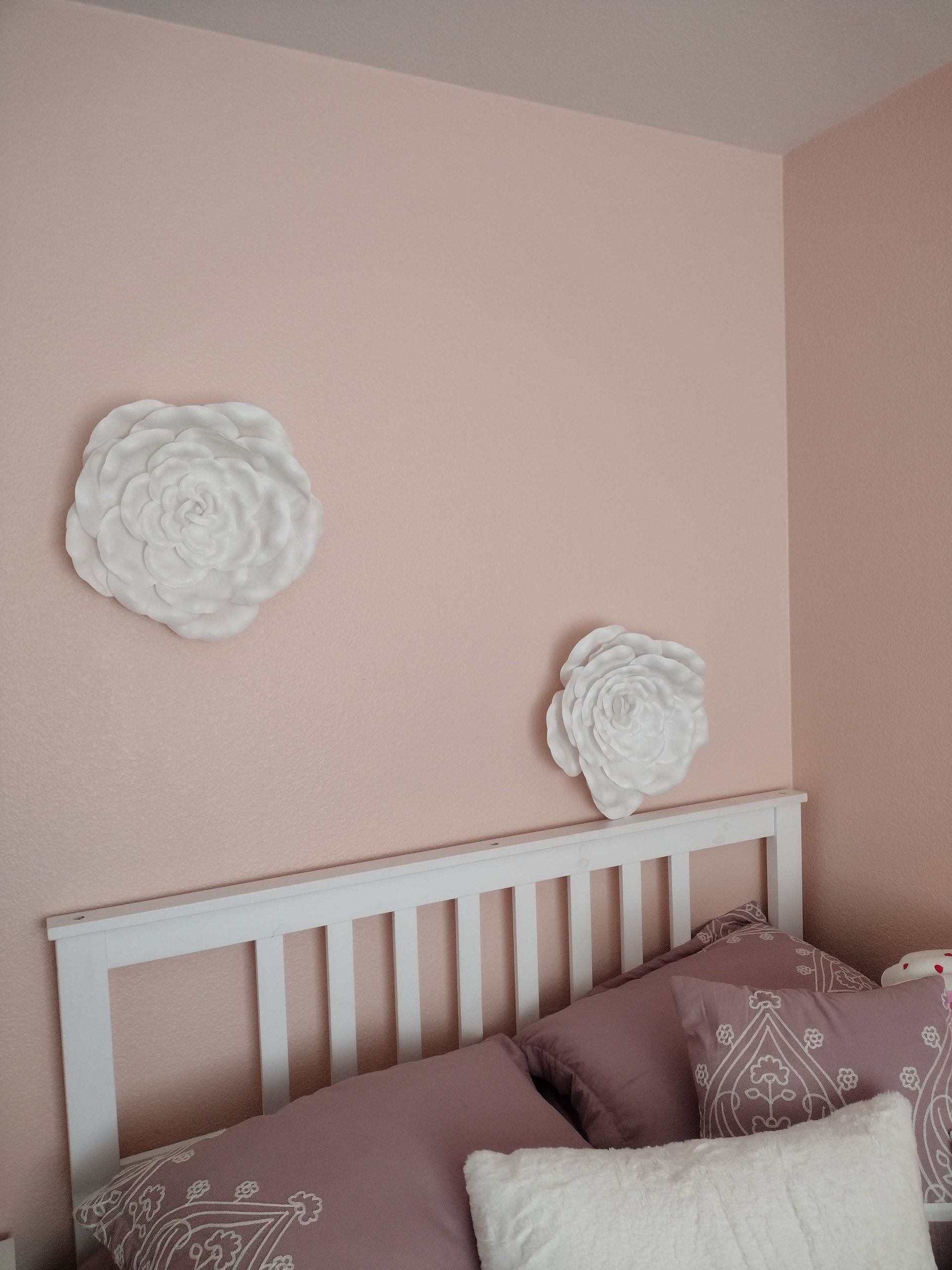 Pink bedroom corner with a white bed, mauve bedding, and two white floral wall decorations.