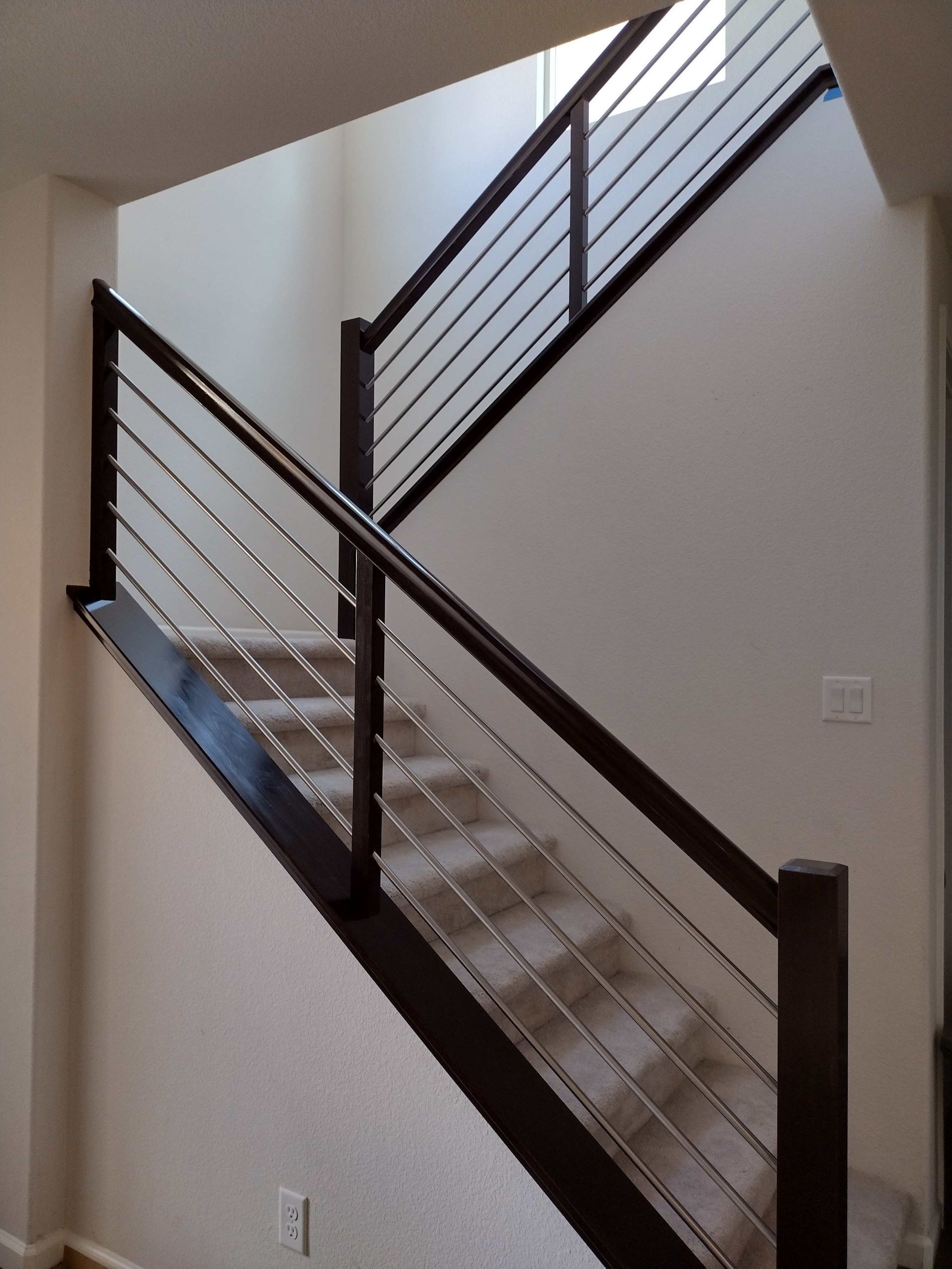 Indoor staircase with dark wood railings and white walls, viewed diagonally from below