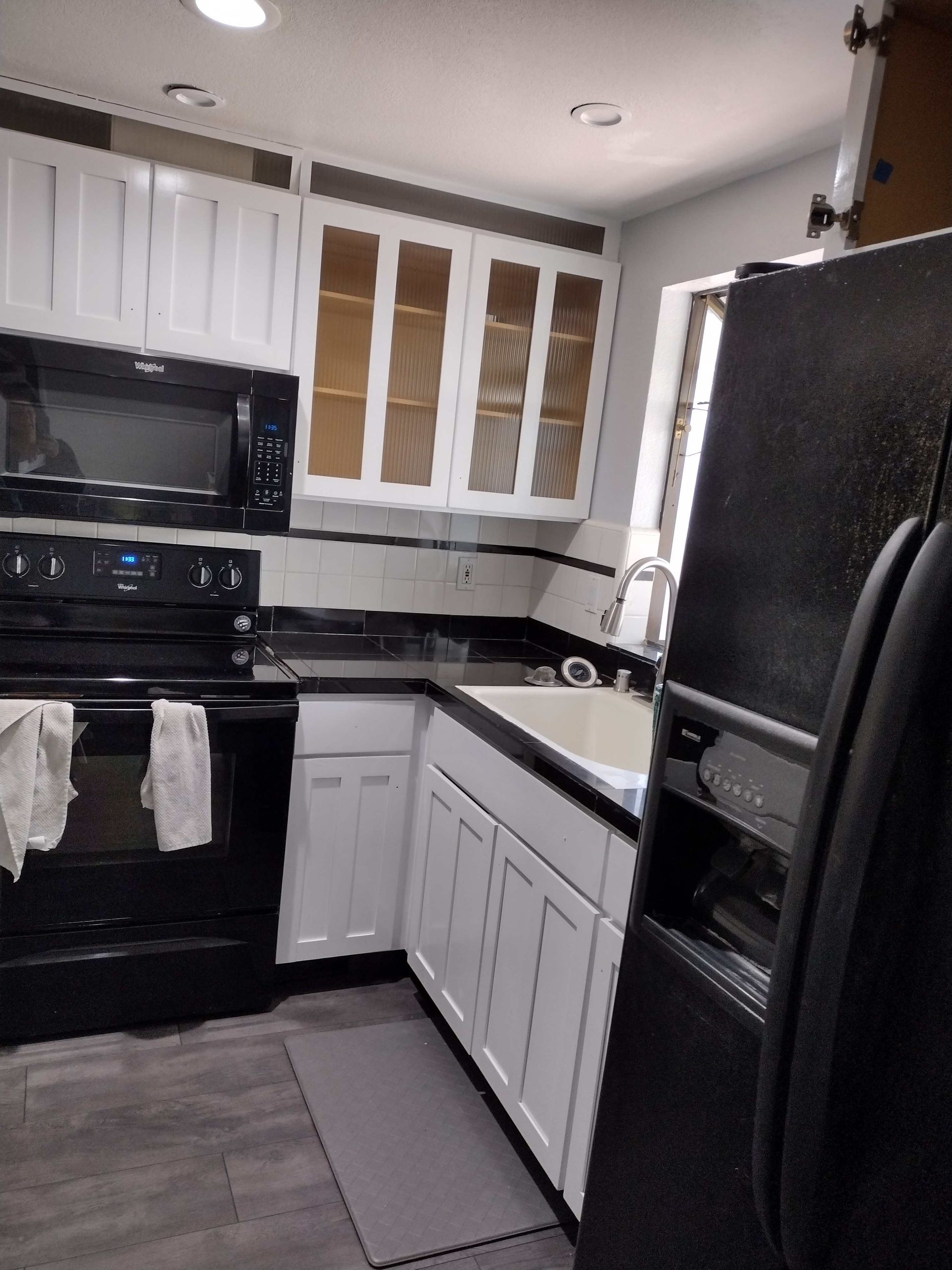 A kitchen featuring white cabinets, black appliances, dark countertops, and light gray wood-look flooring.