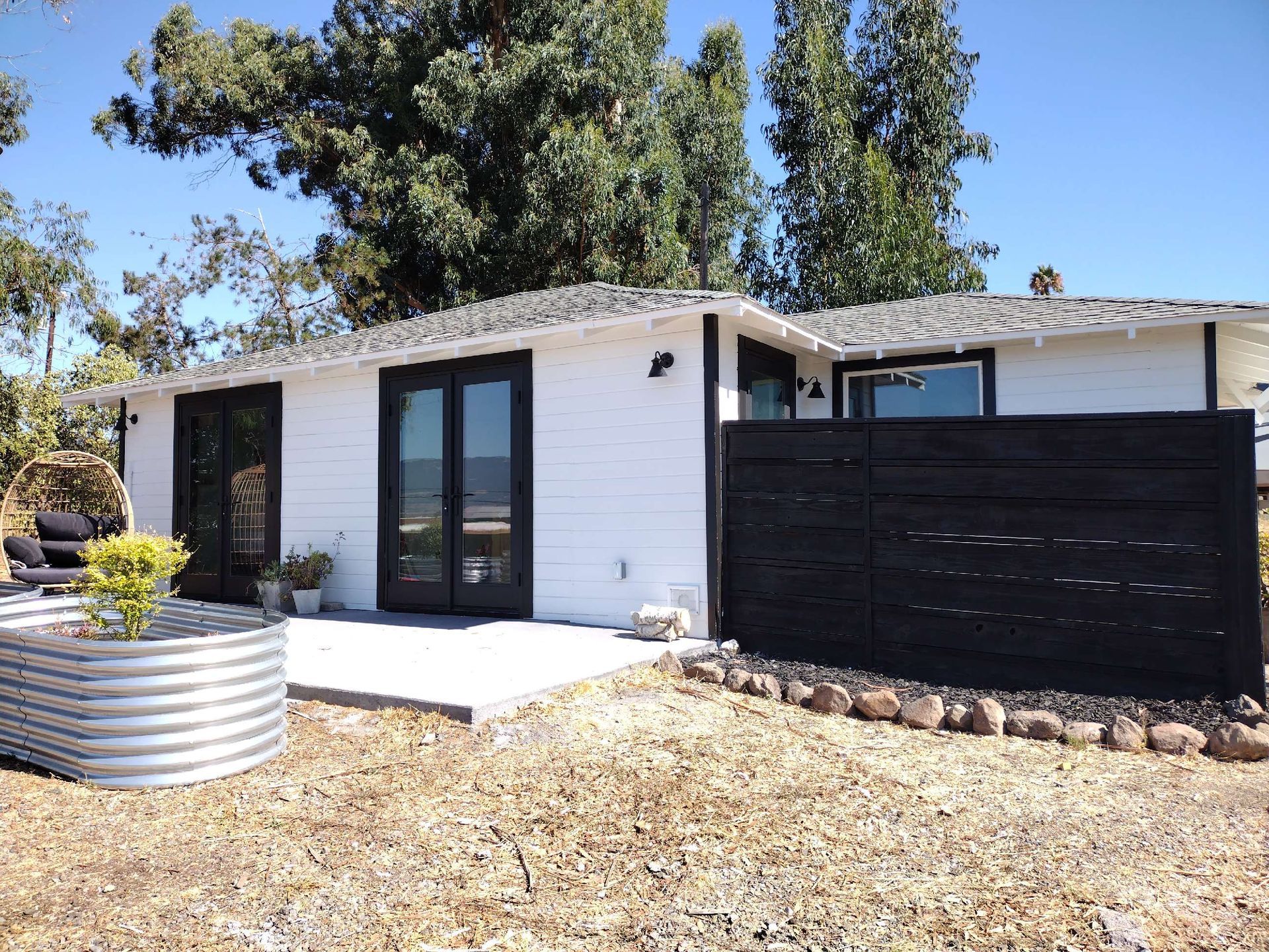 A person in a plaid shirt and cap uses a long-handled roller to paint a wall grey in a room under renovation.